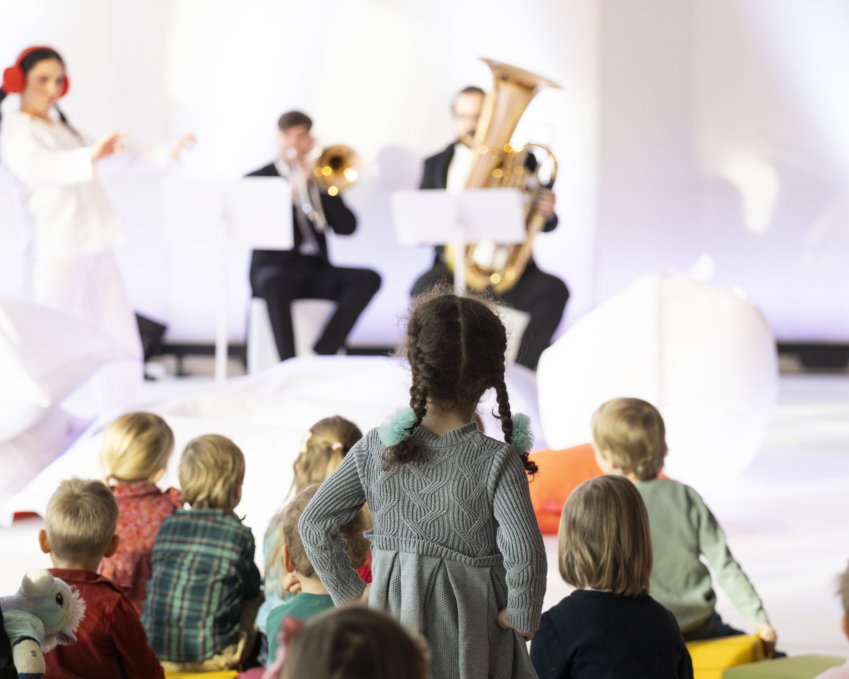 Kinder im Publikum, zwei Musiker spielen Musik, zwei Frauen in weißen Anzügen