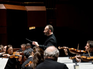 Dirigent Kirill Petrenko leitet das Orchester, während die Musiker konzentriert ihre Streichinstrumente spielen.