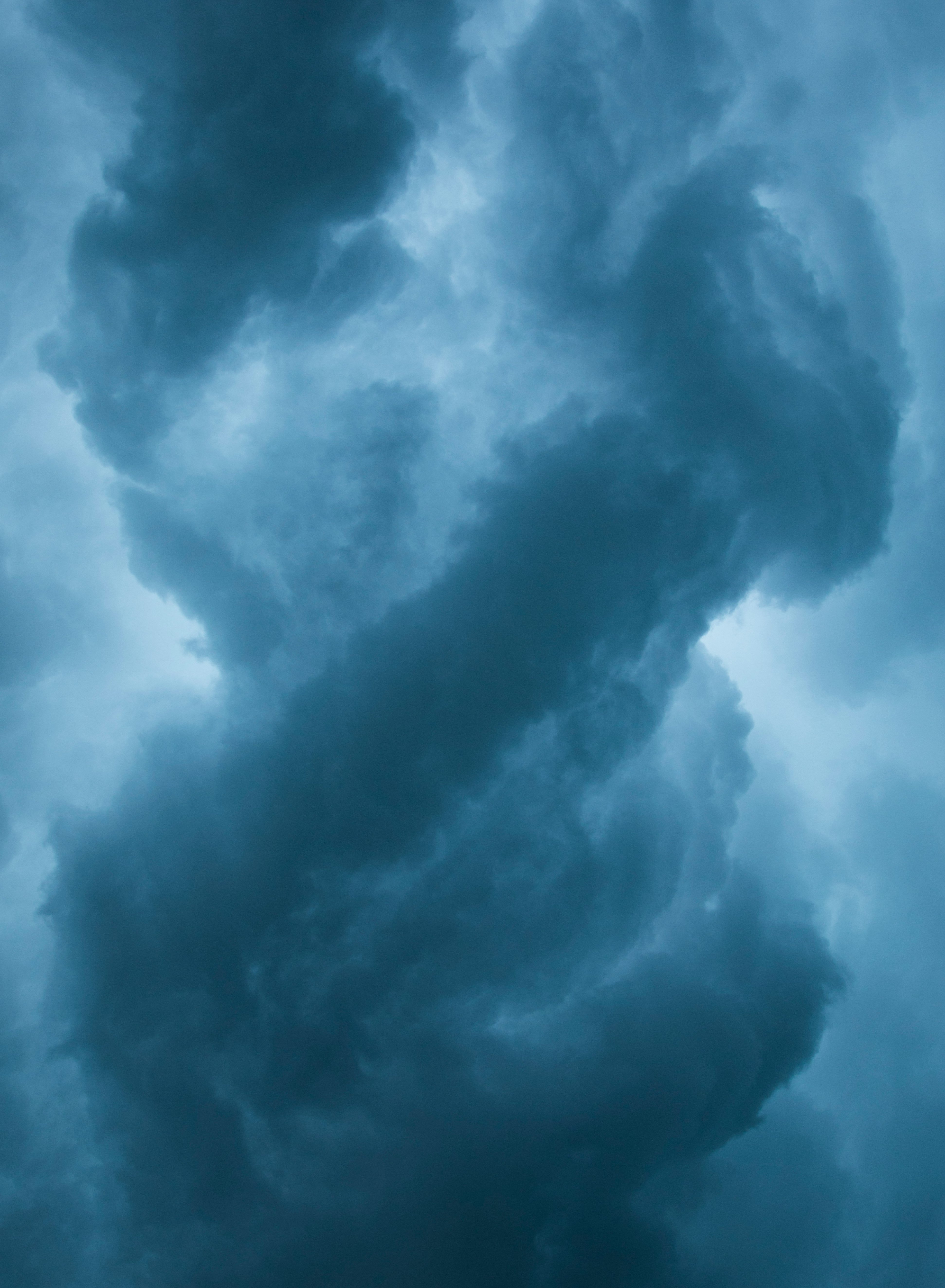 Dunkle, wirbelnde Gewitterwolken bedecken den Himmel und werden von einem schwachen Licht im Hintergrund beleuchtet, wodurch eine dramatische und stimmungsvolle Atmosphäre mit Blau- und Grautönen entsteht.