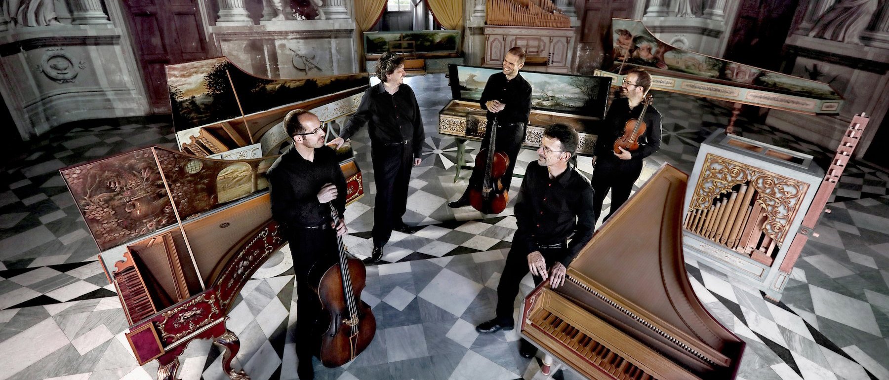 Fünf Musiker in einem prächtigen, reich verzierten Raum mit Marmorböden, umgeben von Cembalos und anderen historischen Tasteninstrumenten, in schwarzer Kleidung und mit ihren Instrumenten in den Händen.