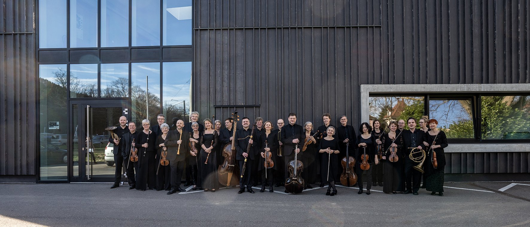 Das Orchester steht vor einer mit Holz verkleideten Wand, das Bild ist schwarz-weiß.
