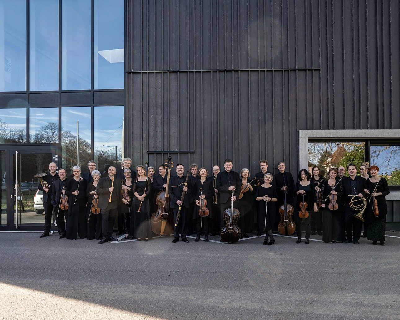 Das Orchester steht vor einer mit Holz verkleideten Wand, das Bild ist schwarz-weiß.