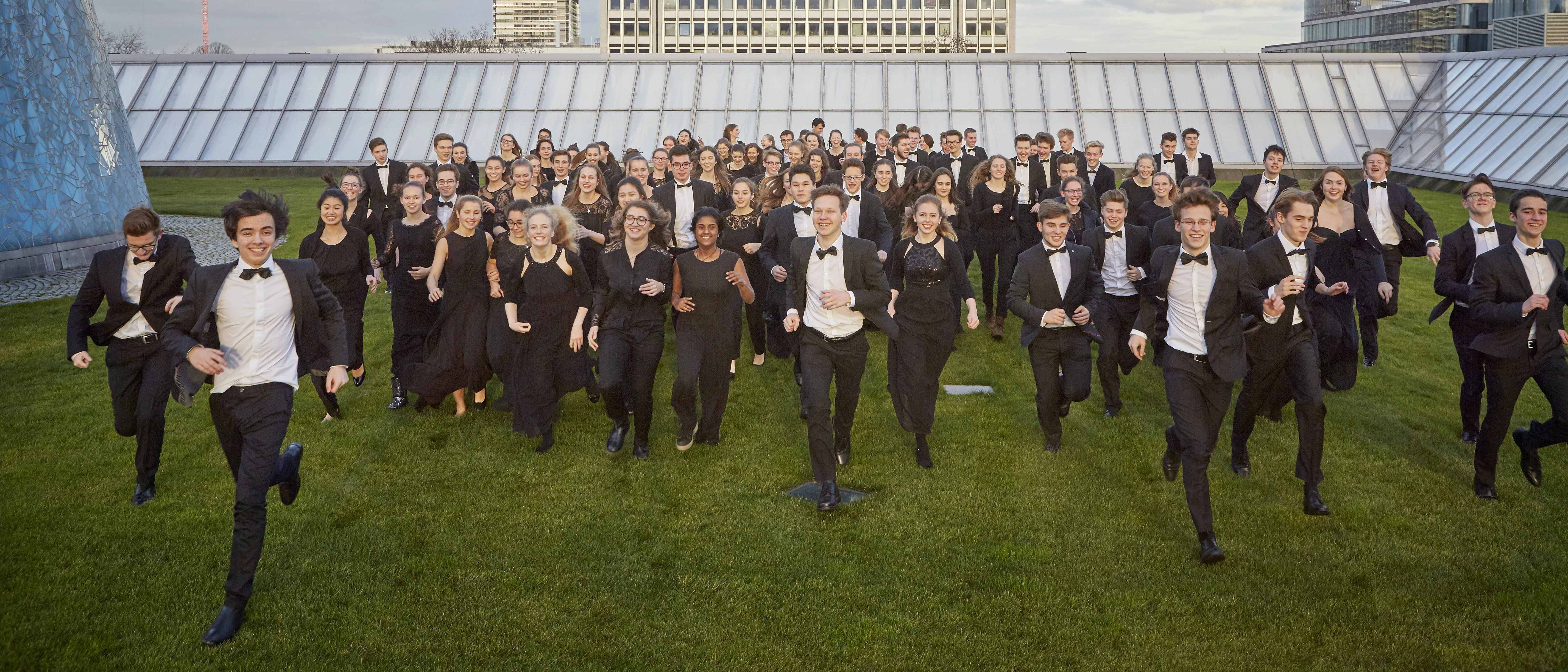 Young people in orchestral dress run towards the camera on a green skyscraper roof