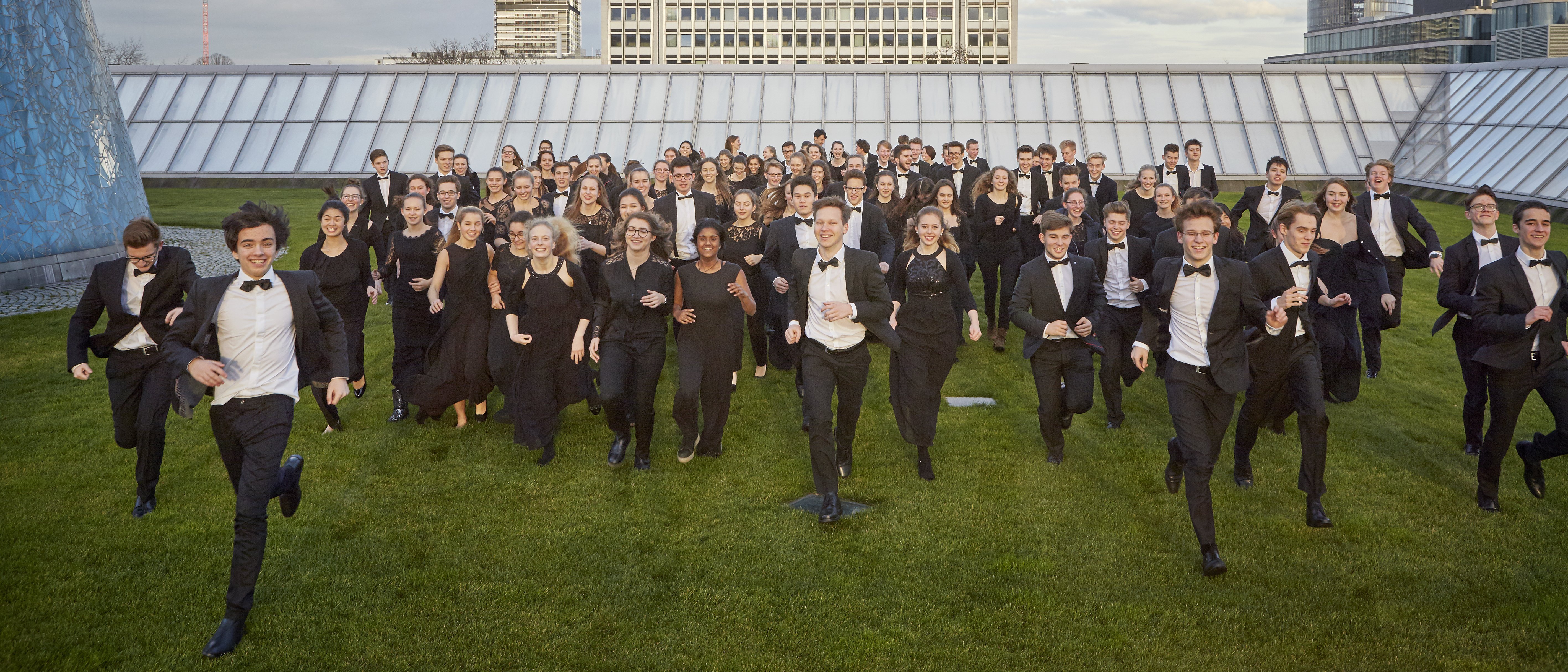 Young people in orchestral dress run towards the camera on a green skyscraper roof