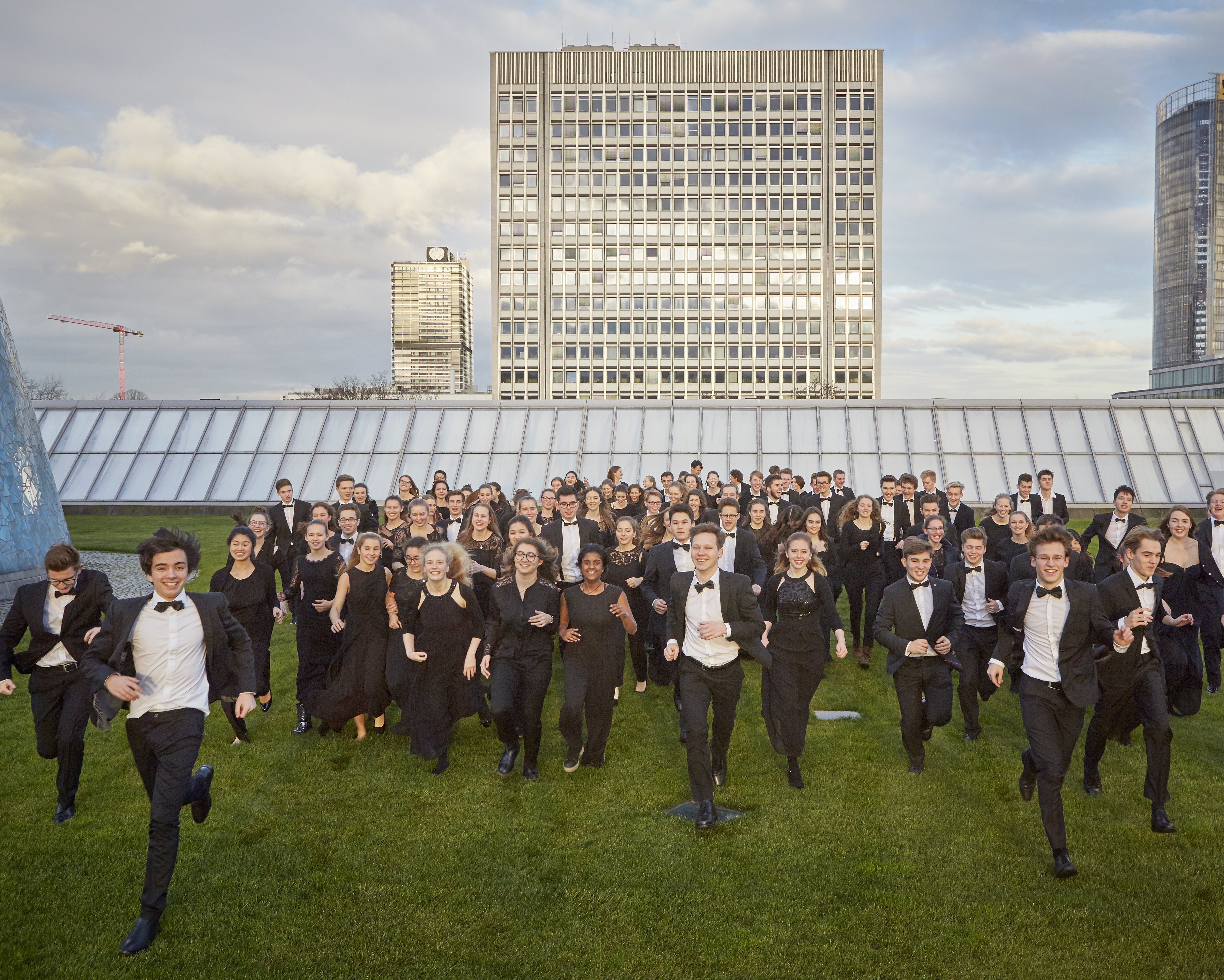 Jugendliche in Orchesterkleidung rennen auf einem begrünten Hochhausdach auf die Kamera zu