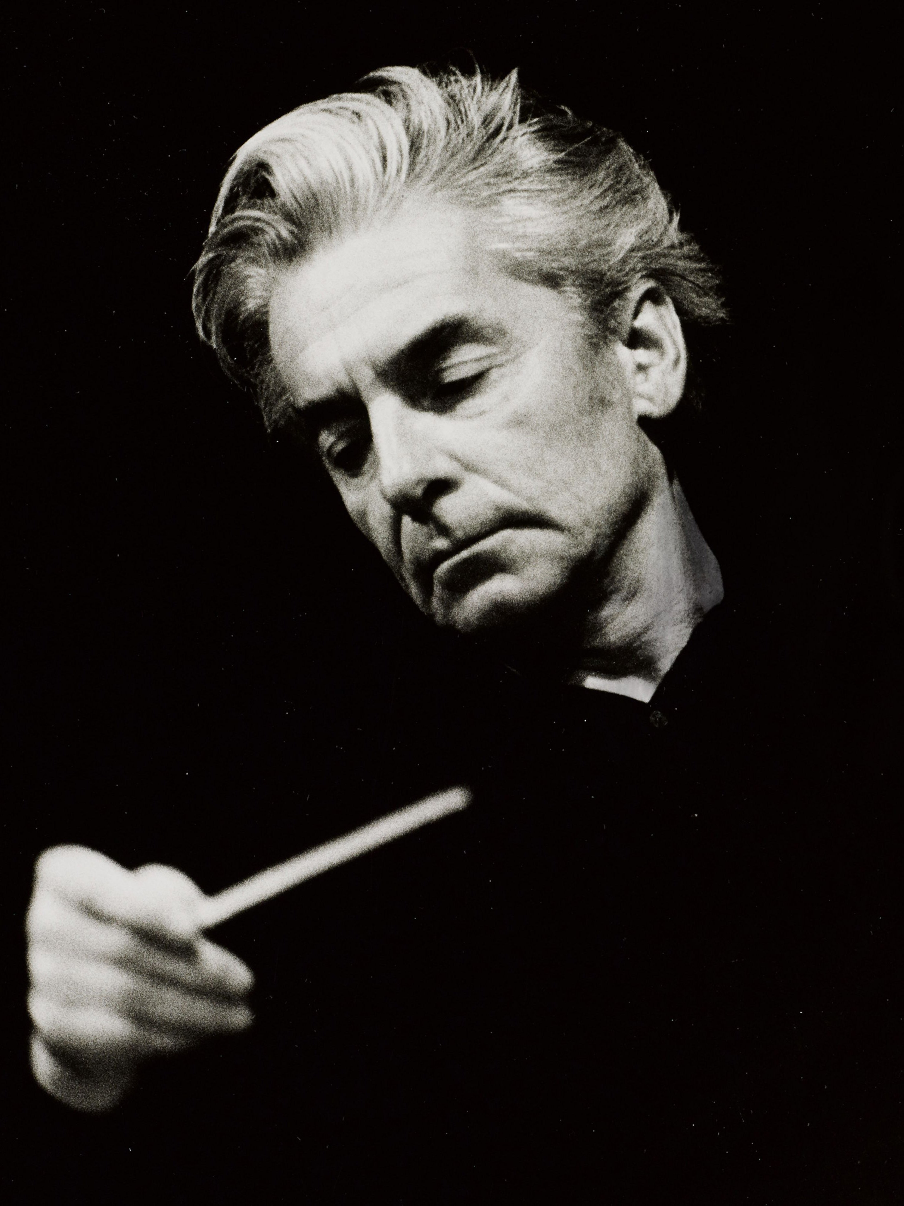 Herbert von Karajan, zur Seite blickend, mit Taktstock in der Hand.