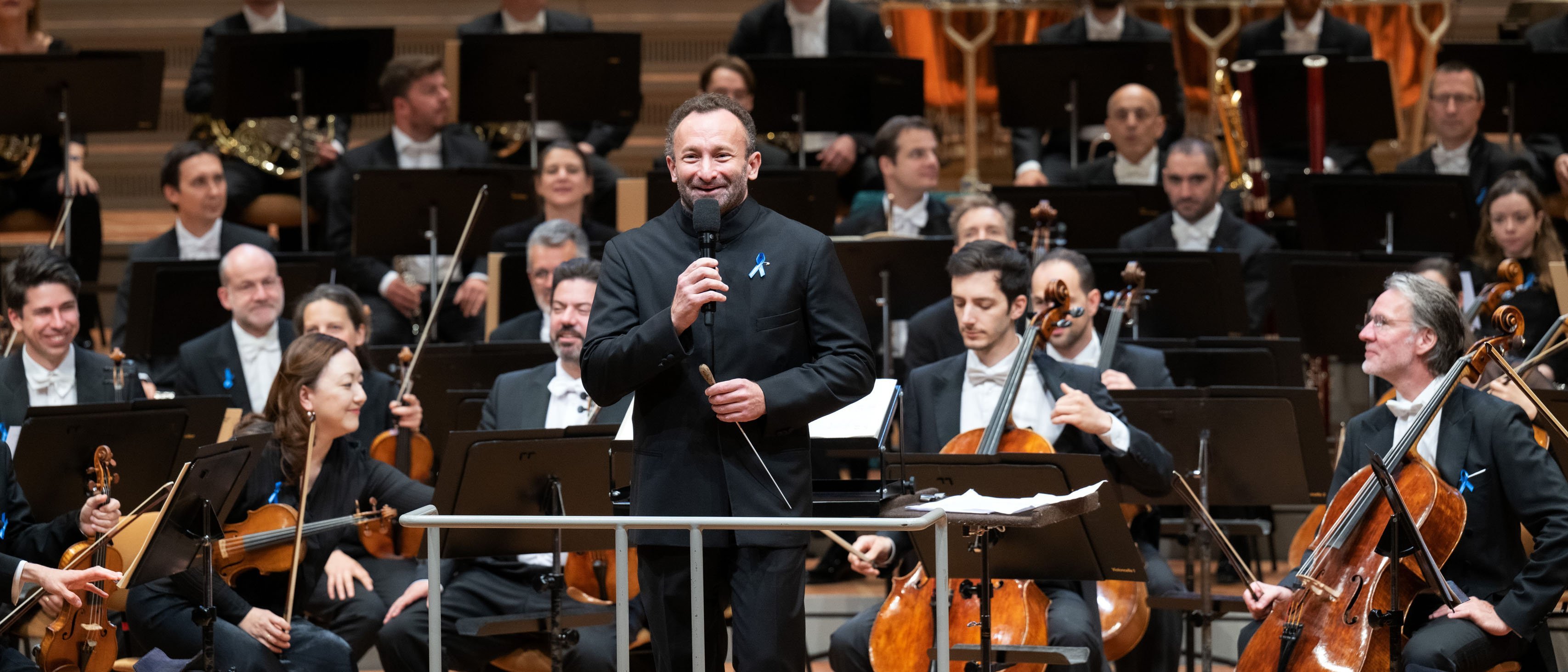 Kirill Petrenko with microphone in front of the orchestra