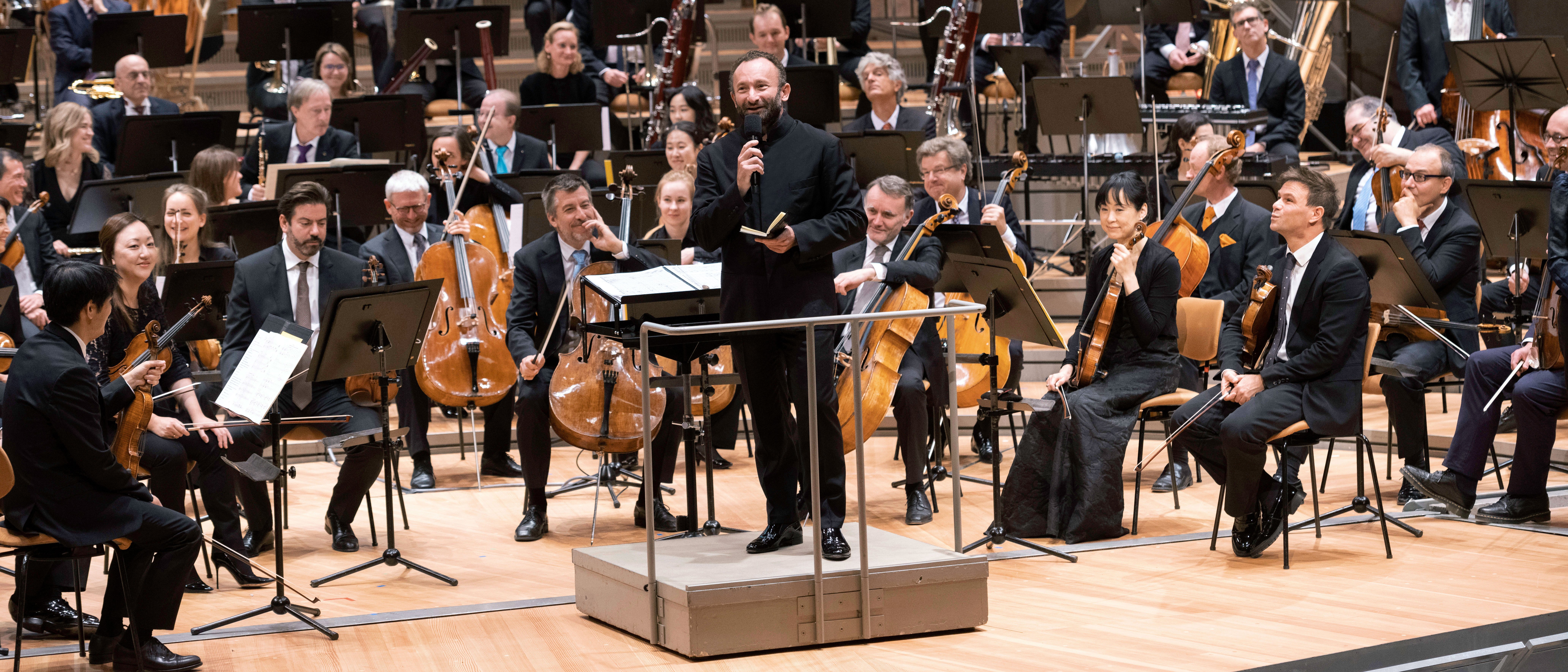 Kirill Petrenko mit Mikrophon vor dem Orchester