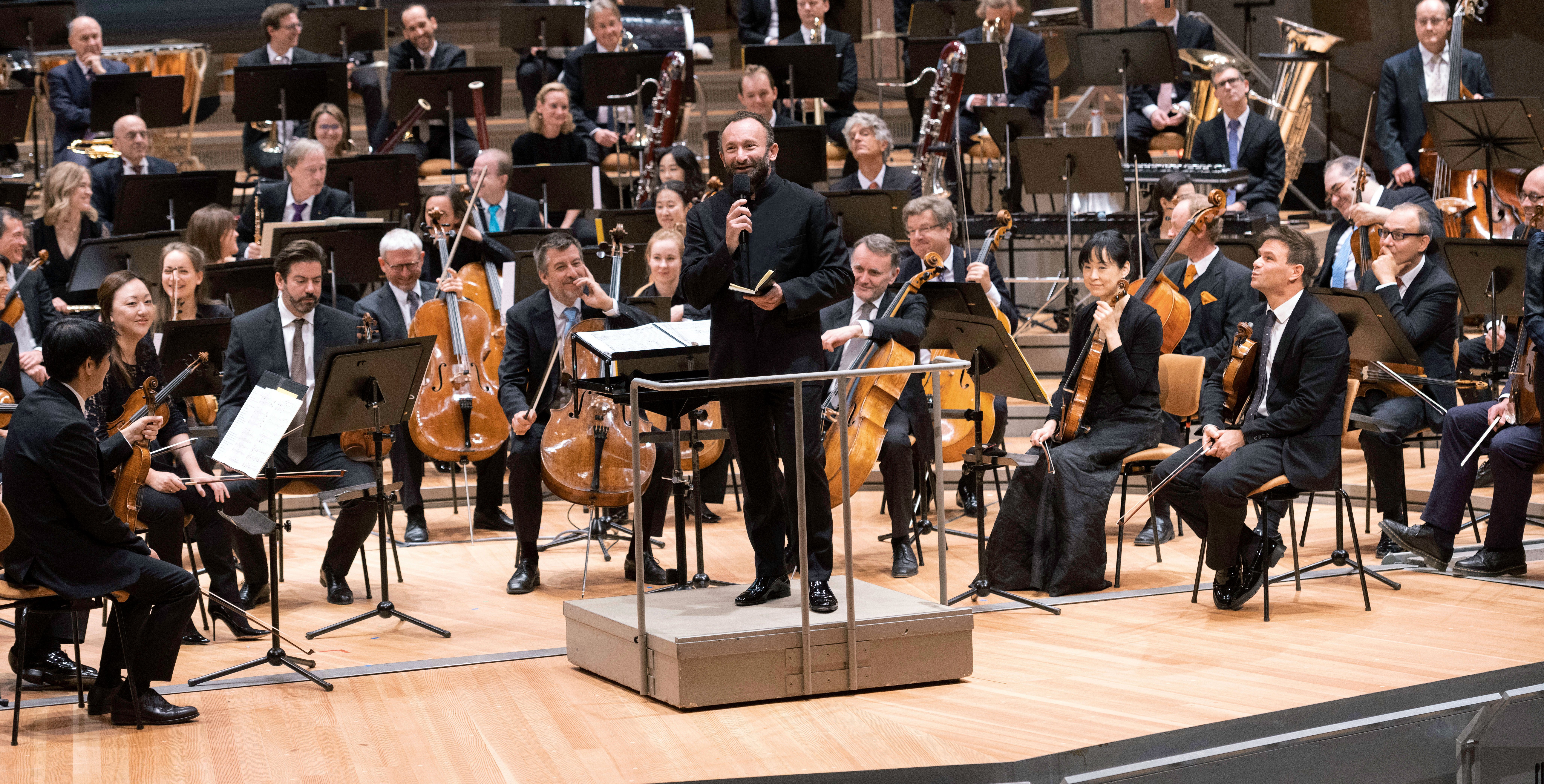 Kirill Petrenko with microphone in front of the orchestra