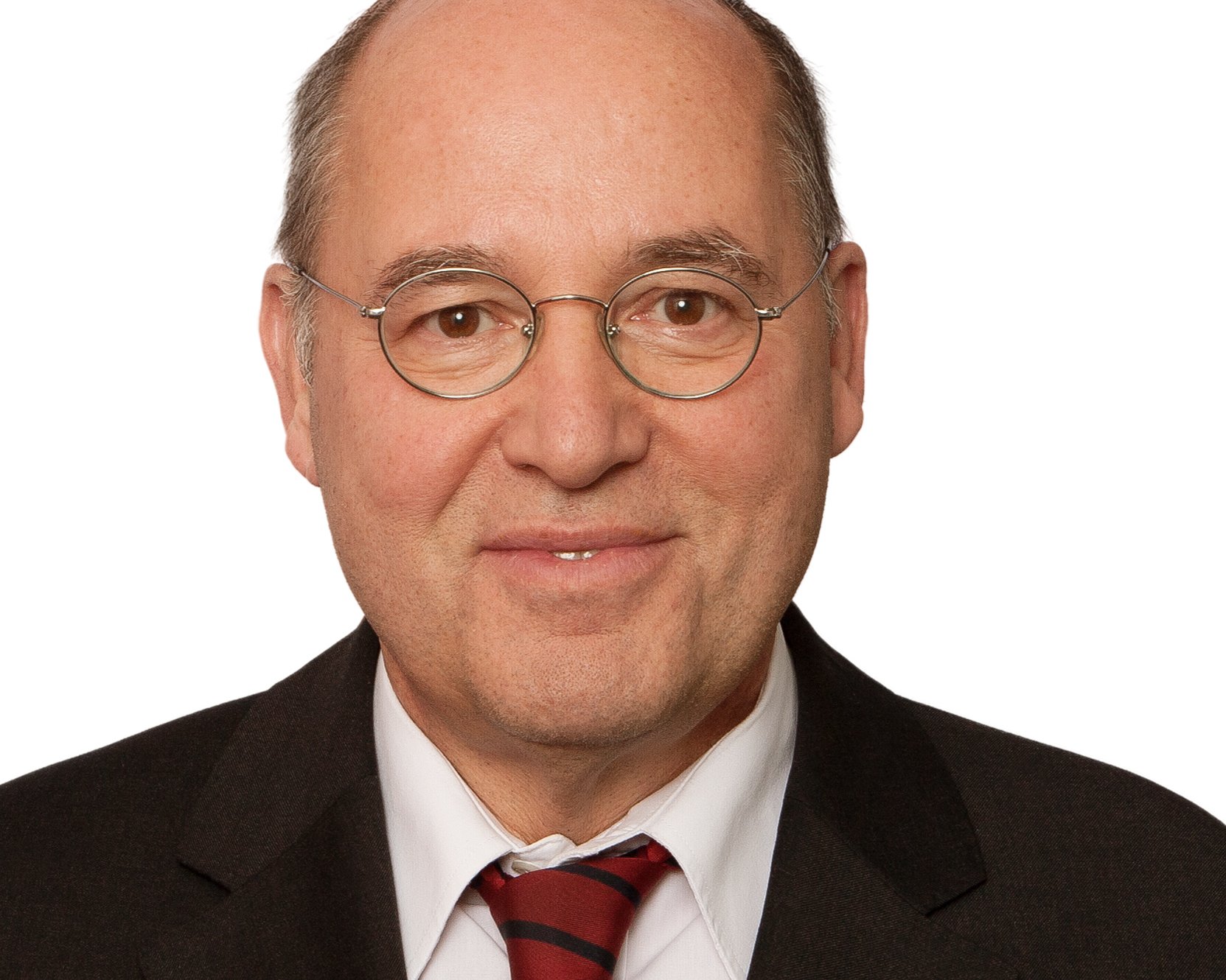 Bald man with glasses, wearing a dark suit, white shirt, and red striped tie, smiling at the camera against a plain white background.
