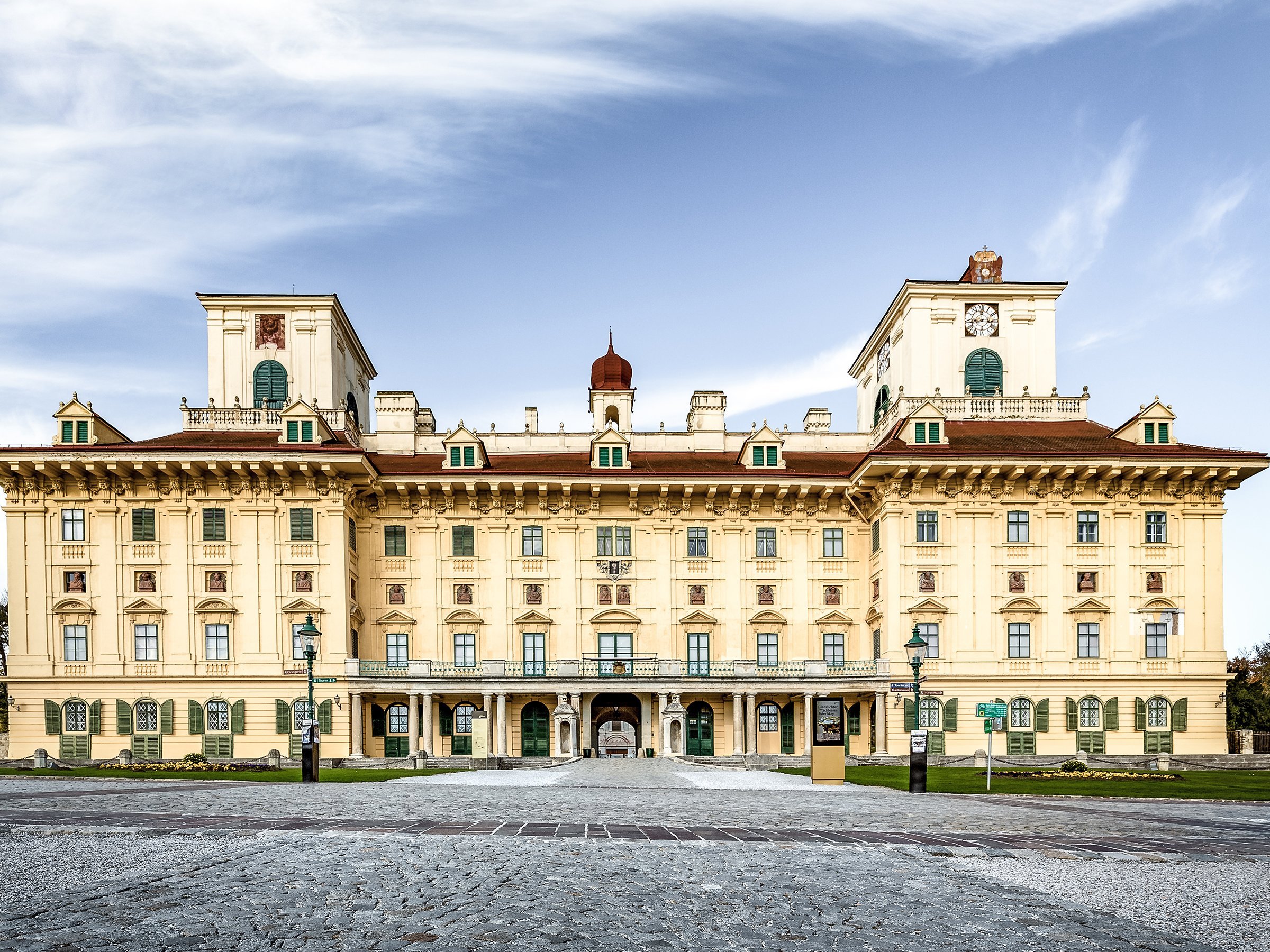 The picture shows a magnificent, ornate building with an elaborate façade, symmetrical design and a central, arched entrance. It has three towers with clocks and stands against a bright blue sky.