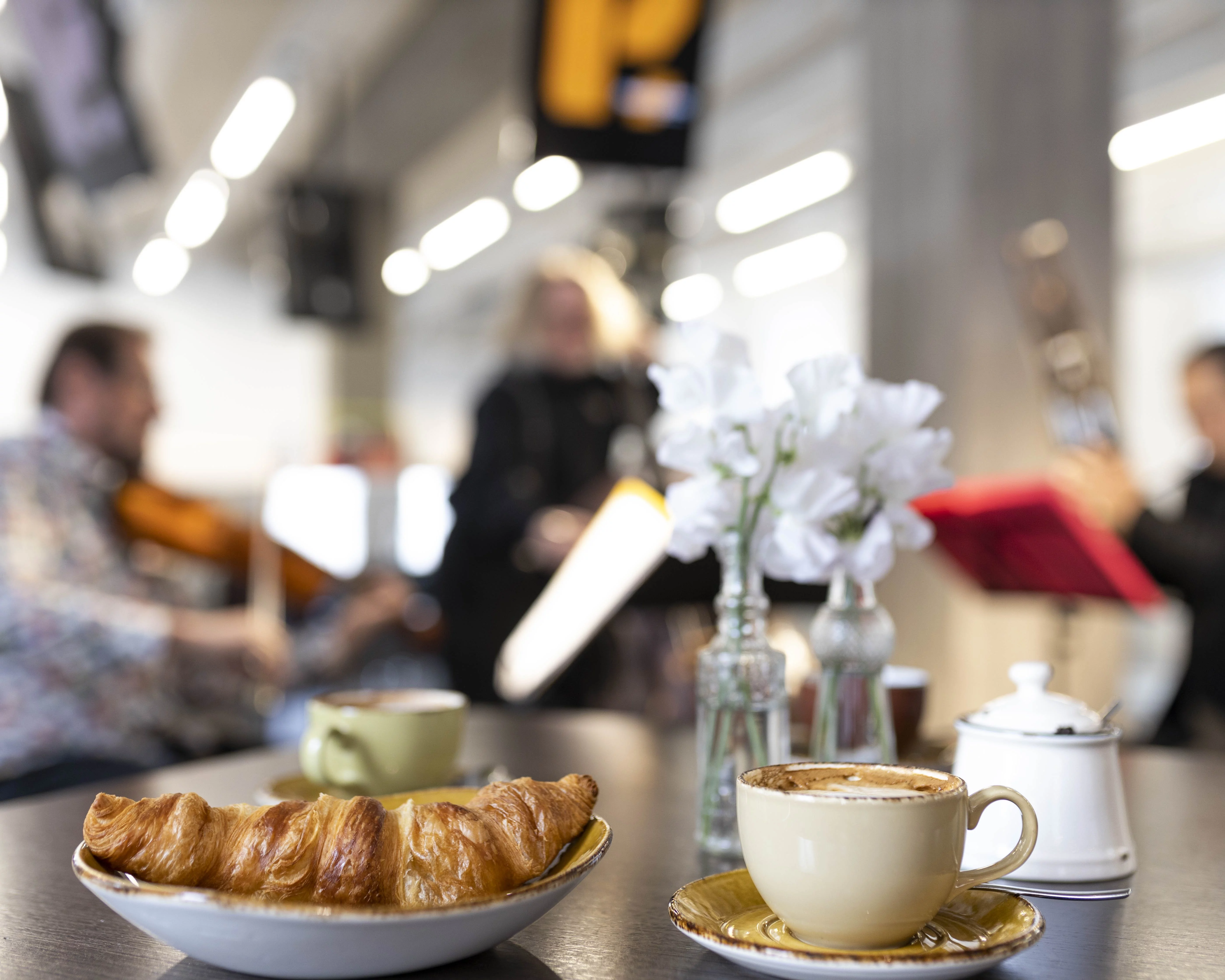 Croissant und Kaffee auf einem Tisch, im Hintergrund spielen Musiker