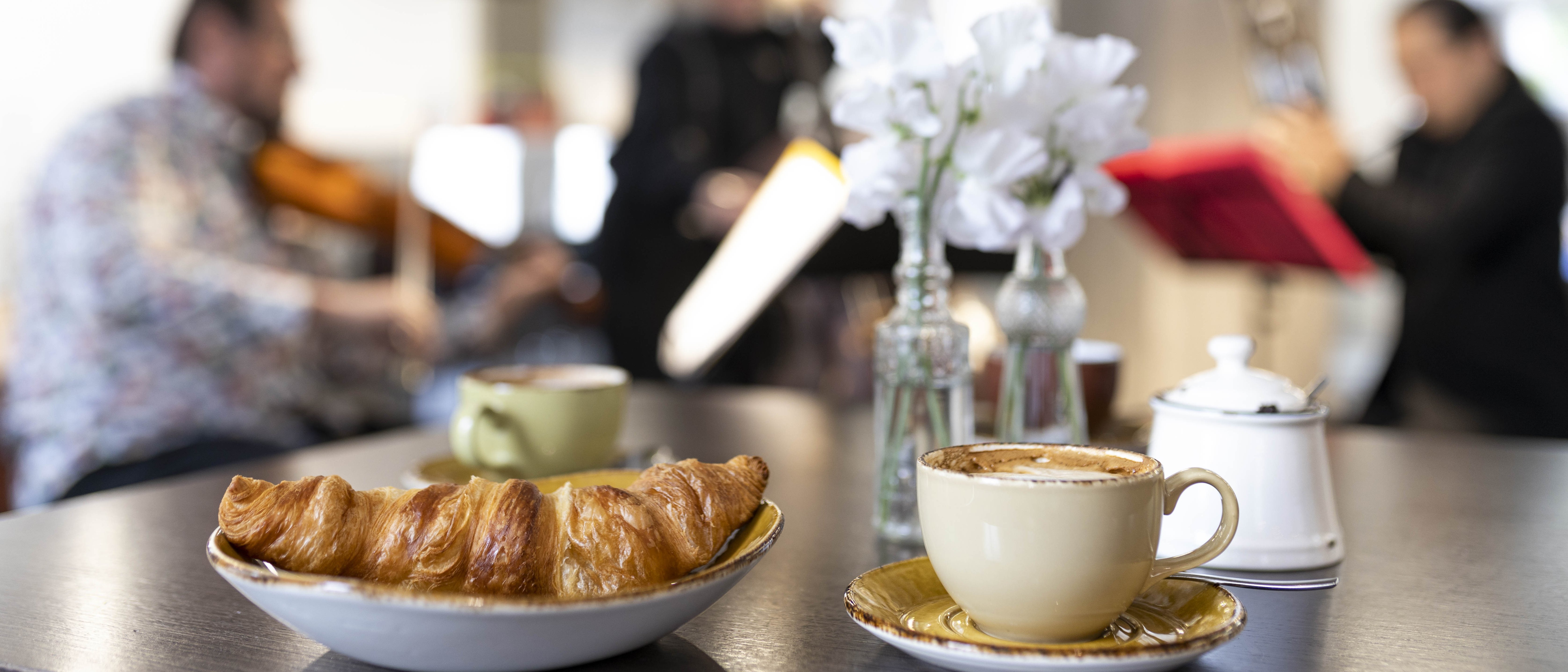 Croissant und Kaffee auf einem Tisch, im Hintergrund spielen Musiker