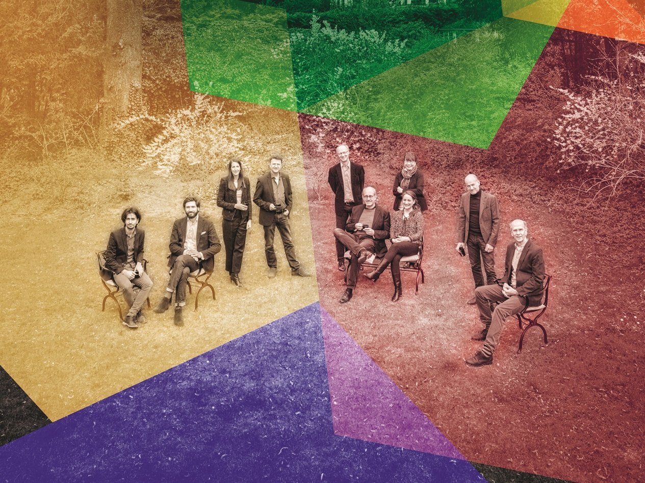 Eight people sit on chairs in an outdoor setting with trees and a building in the background. The image is overlaid with colorful, semi-transparent geometric shapes.
