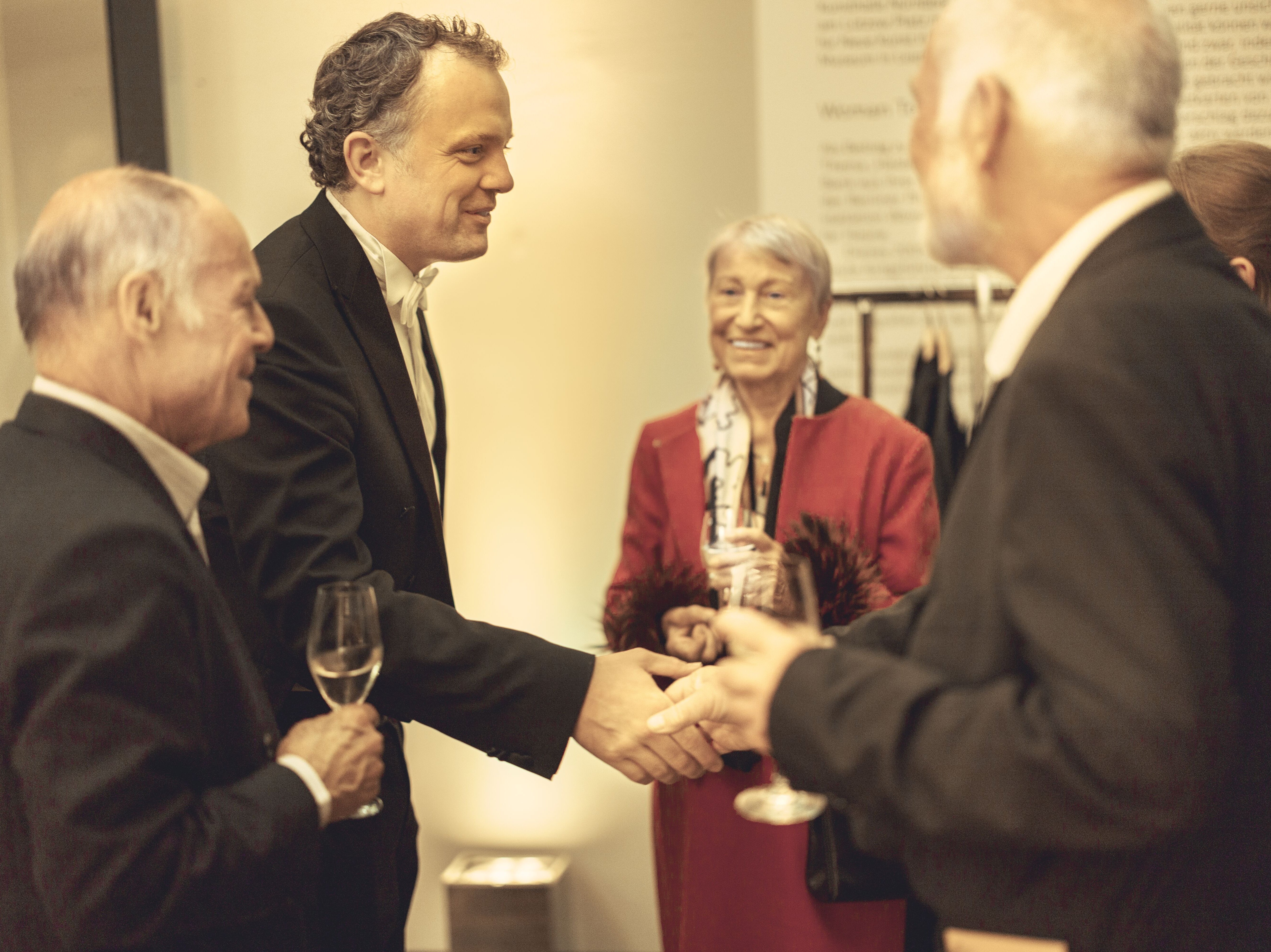 People stand together with a glass of champagne. A man shakes hands with someone