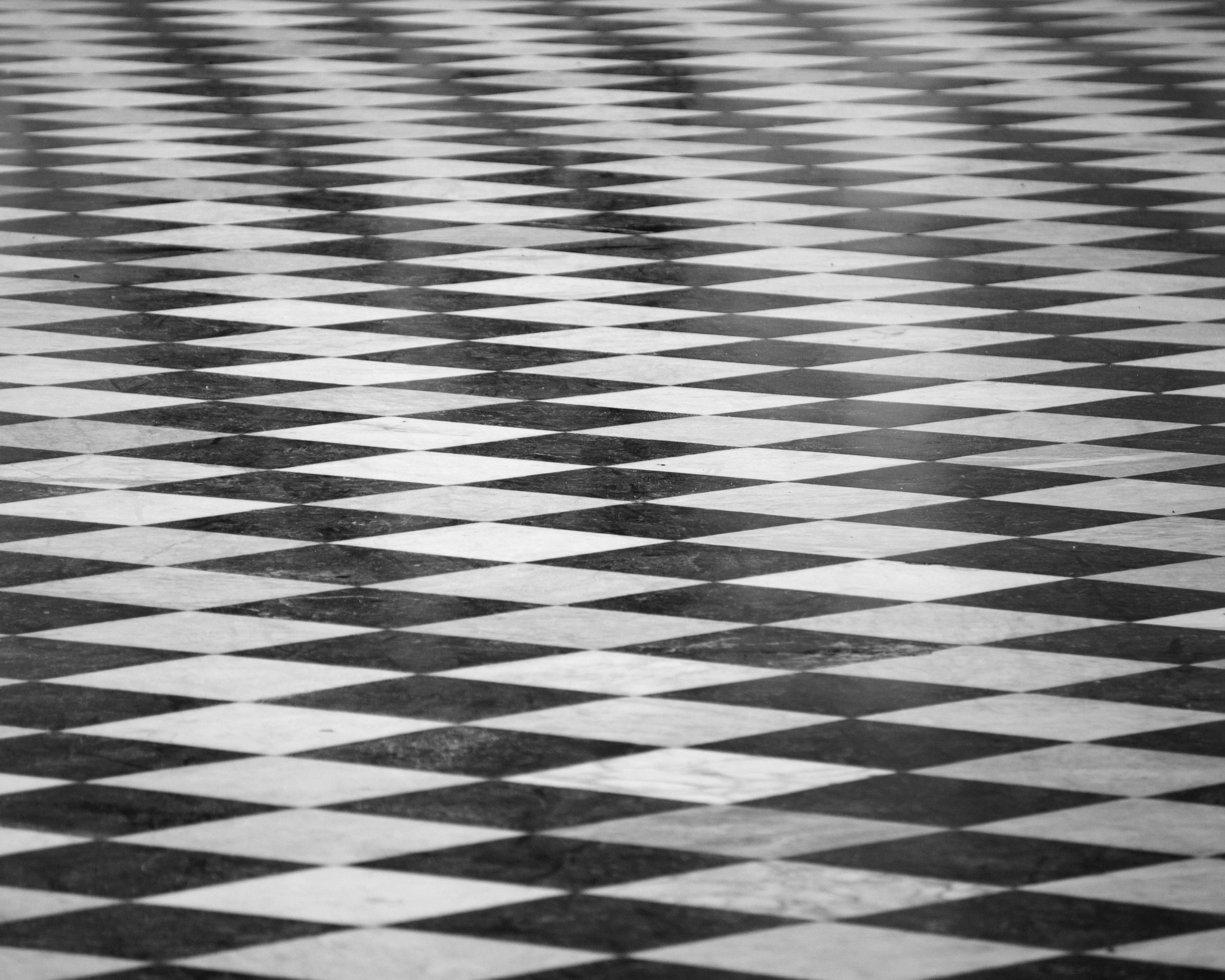 Schwarz-weiß gefliester Boden mit einem sich wiederholenden Rautenmuster, das einen optischen Täuschungseffekt erzeugt. Die Perspektive zeigt das Muster, das sich in die Ferne zurückzieht.