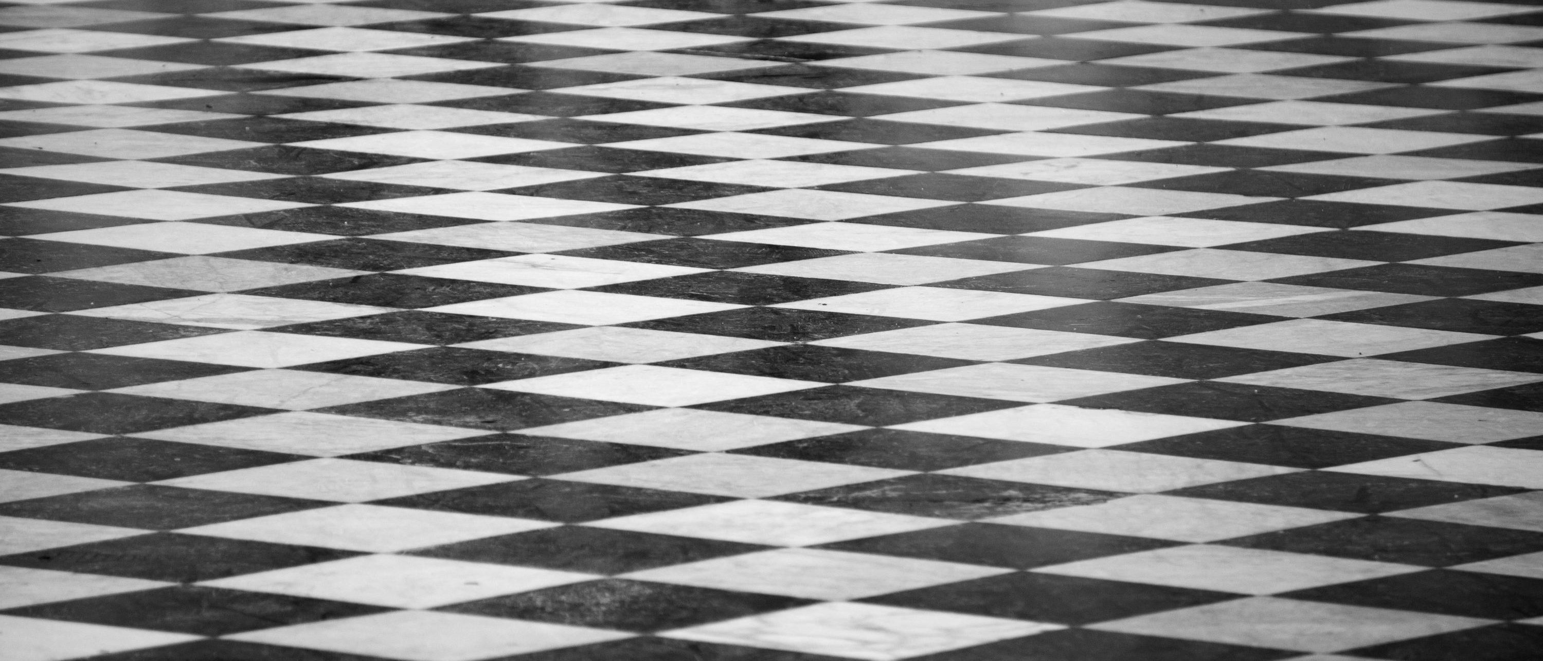 Schwarz-weiß gefliester Boden mit einem sich wiederholenden Rautenmuster, das einen optischen Täuschungseffekt erzeugt. Die Perspektive zeigt das Muster, das sich in die Ferne zurückzieht.
