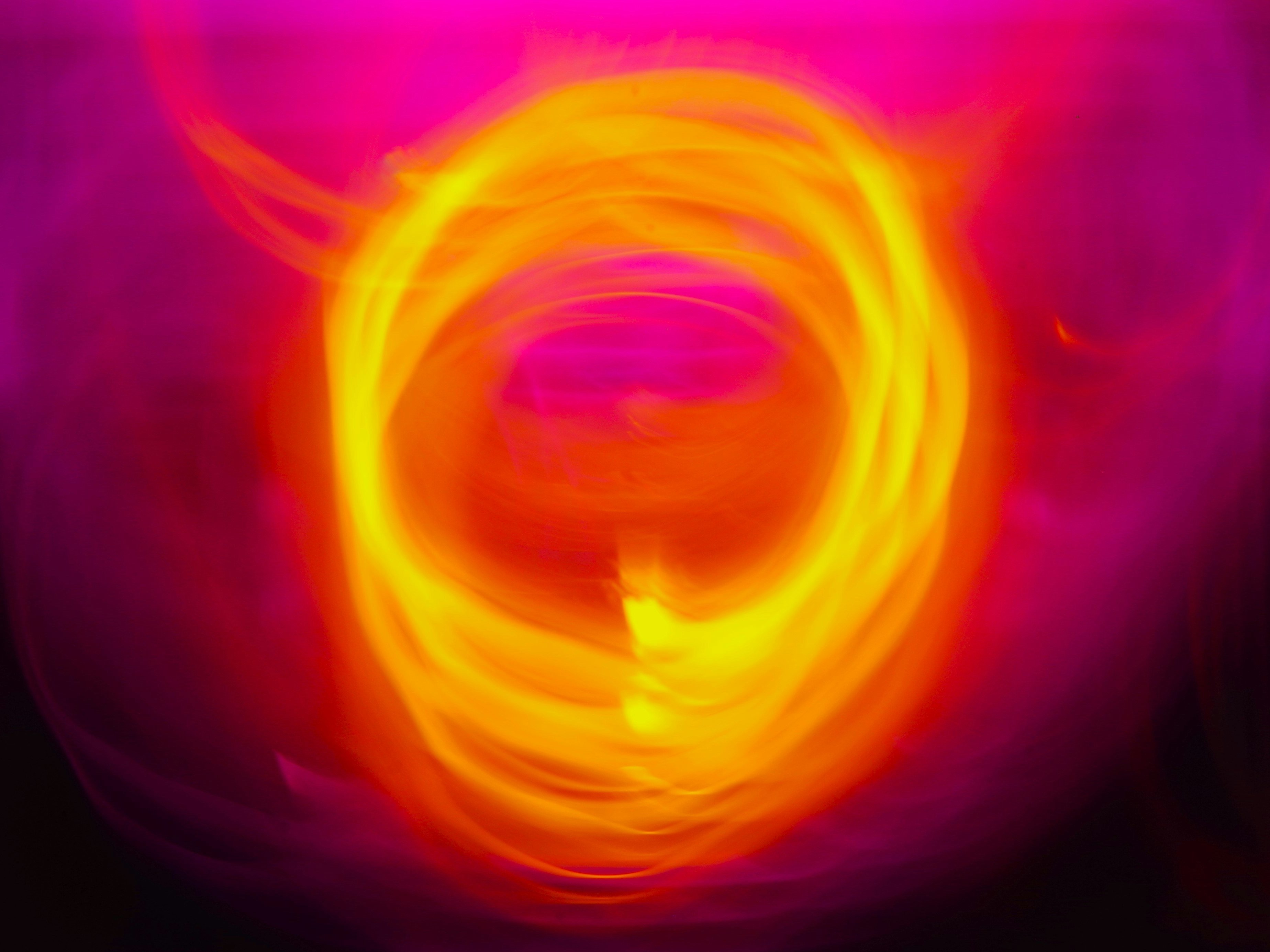 A swirling ring of bright yellow and orange light stands out against a soft, blurred pink and purple background, creating an abstract, fiery effect.
