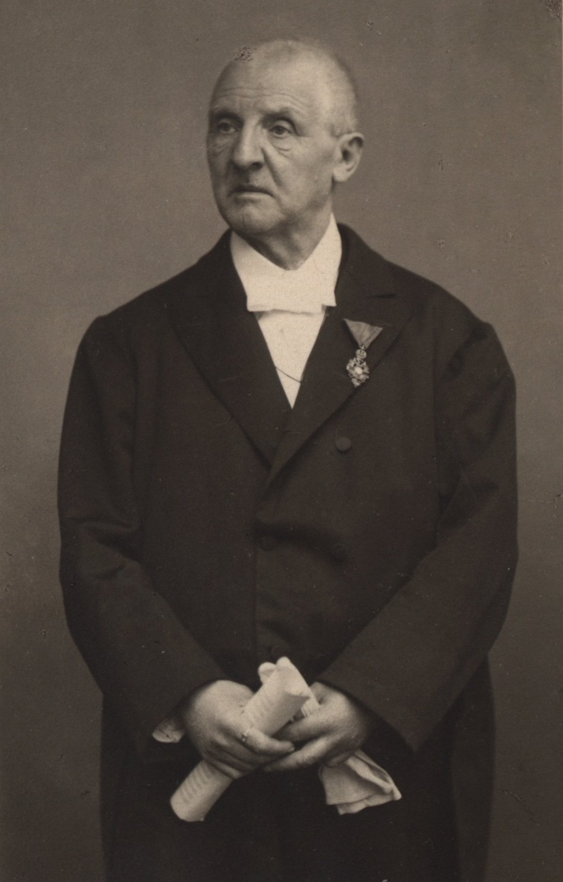 Porträt-Foto von Anton Bruckner. Er blickt zur Seite und hält Dokumente in seiner Hand.
