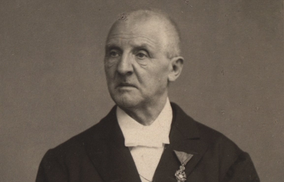 Porträt-Foto von Anton Bruckner. Er blickt zur Seite und hält Dokumente in seiner Hand.