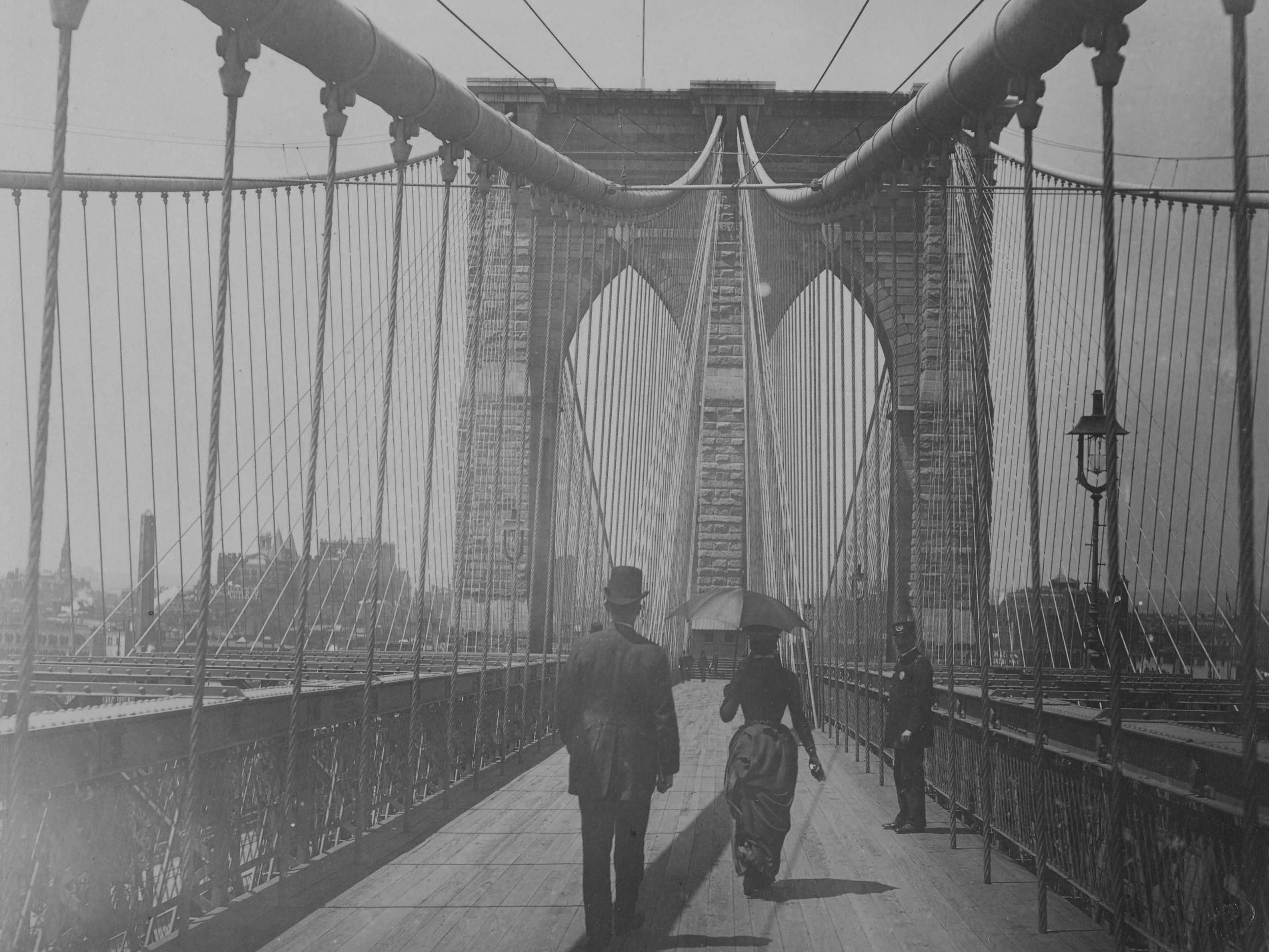 Auf der Brooklyn Bridge. Es sind drei Personen zu erkennen.