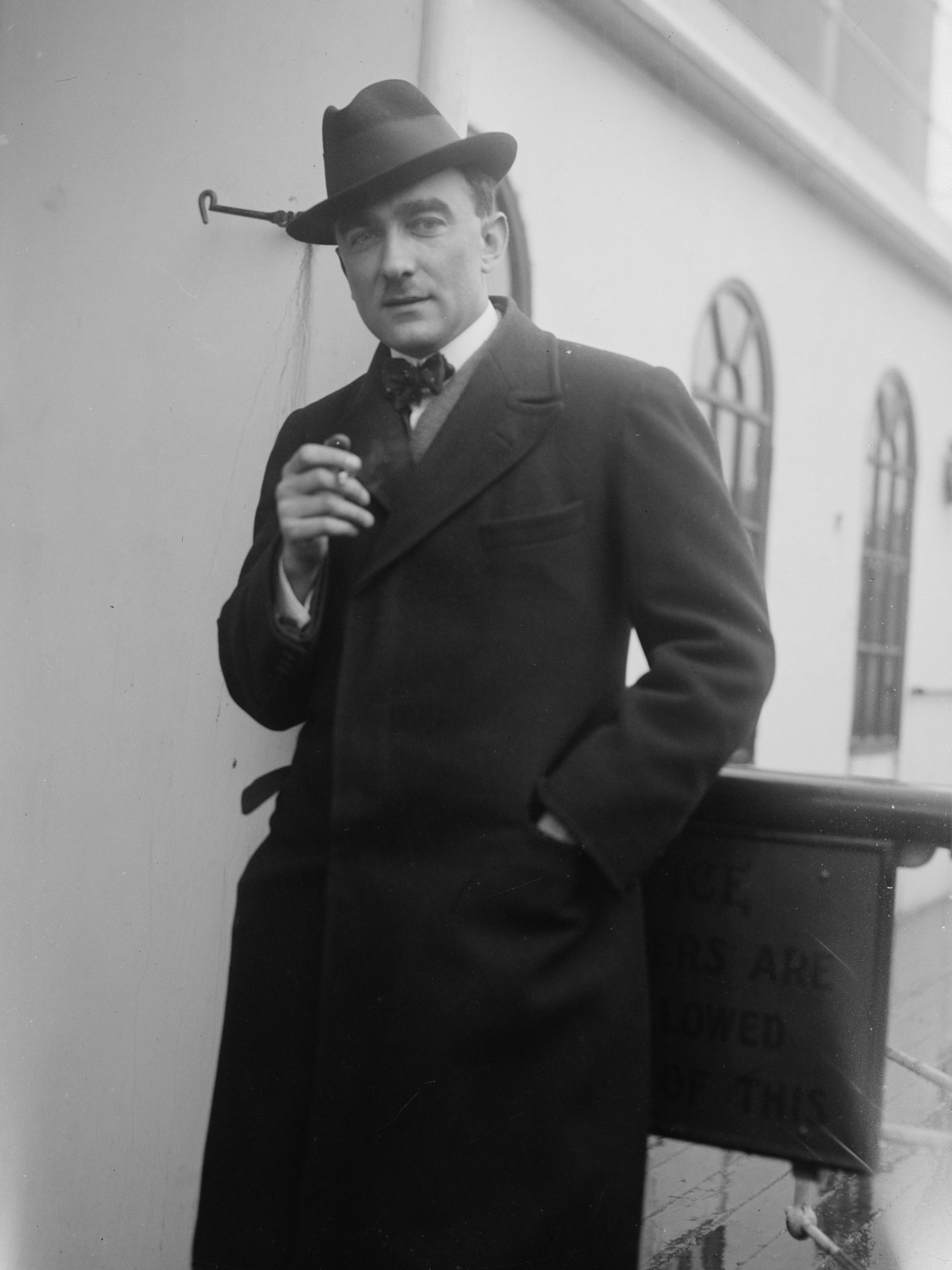 Portrait of Karol Szymanowski. He is wearing a coat and a hat, holding a cigarette in his right hand.