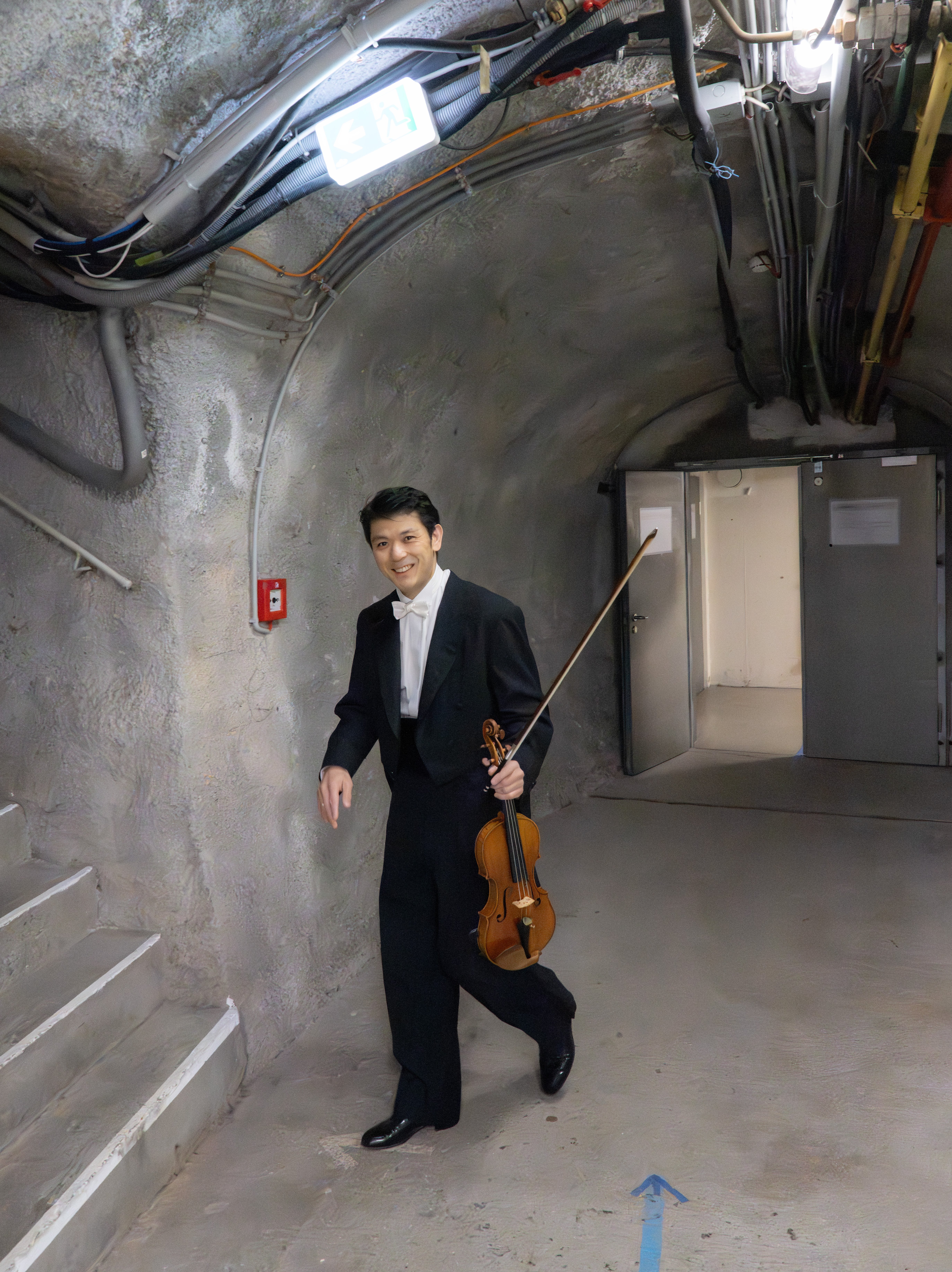 1. Konzertmeister Daishin Kashimoto mit seiner Geige in einem in Stein gemeißelten Tunnel auf dem Weg zum Orchestergraben in der Felsenreitschule.