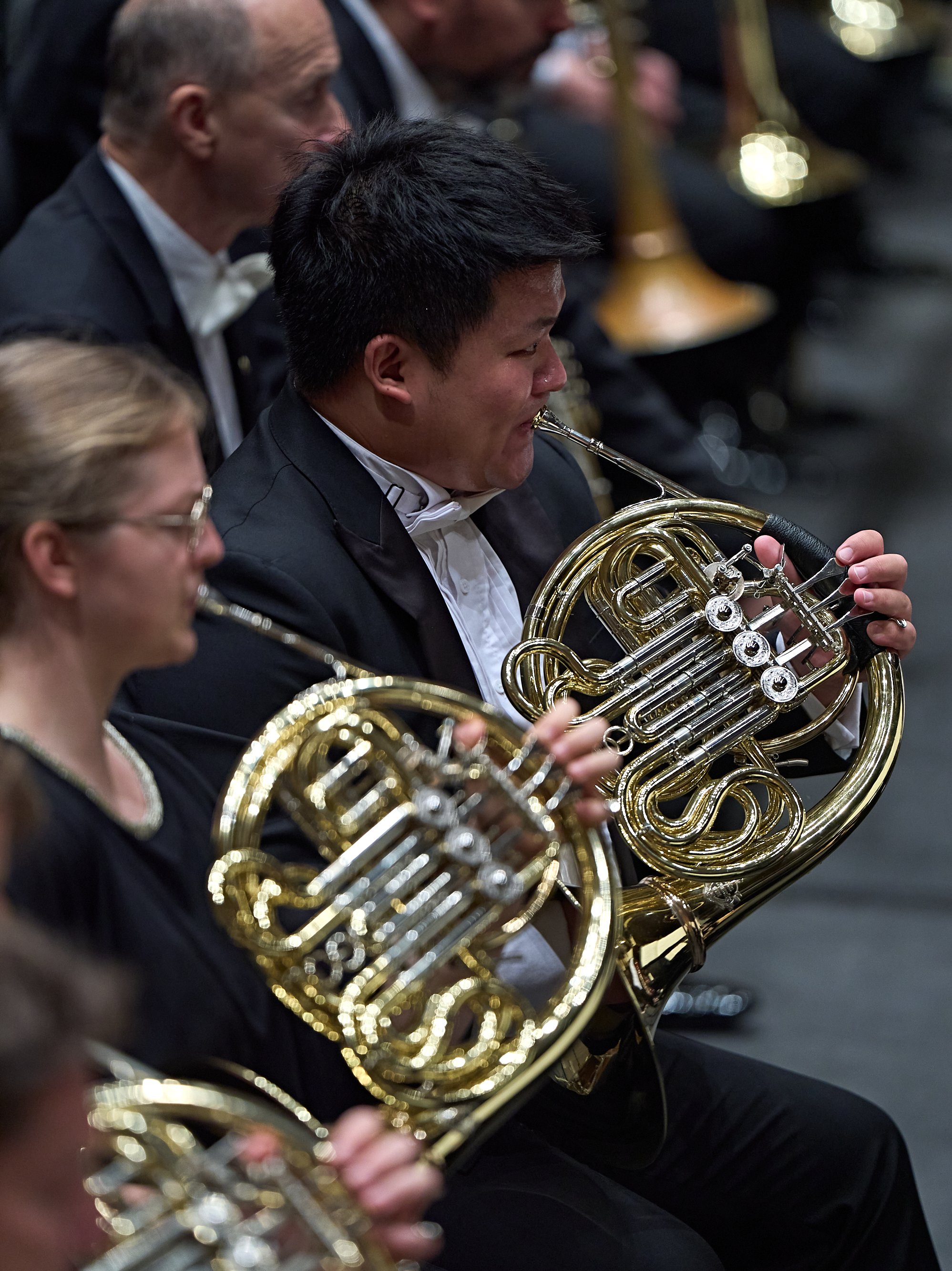 Zwei Hornisten in formeller Konzertkleidung, die in einem Orchester spielen.
