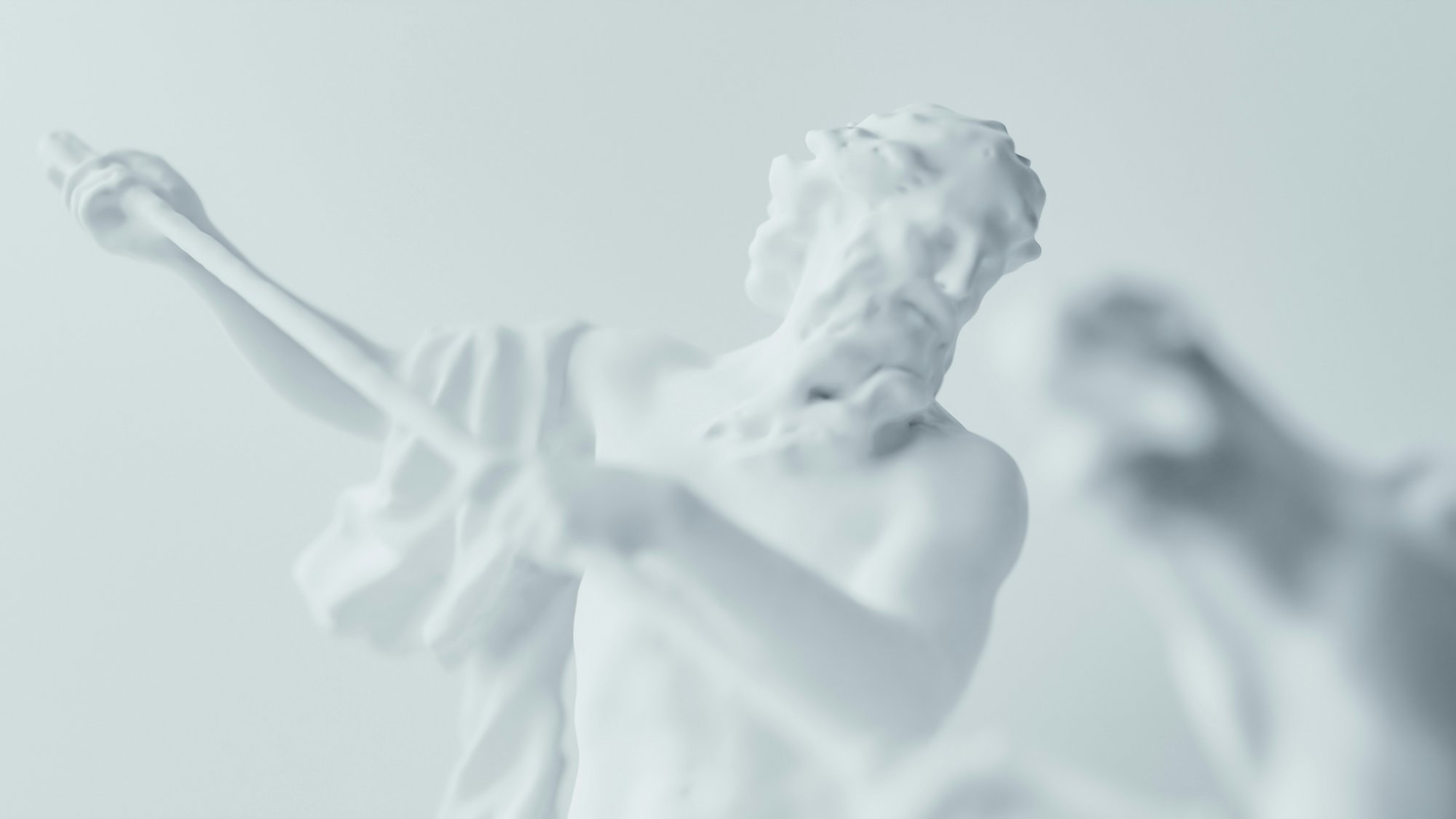 Eine Nahaufnahme einer Statue aus weißem Marmor, die einen bärtigen Mann darstellt, der einen Stab oder Speer hält, mit einer weiteren verschwommenen Gestalt im Vordergrund, alles vor einem hellen Hintergrund.