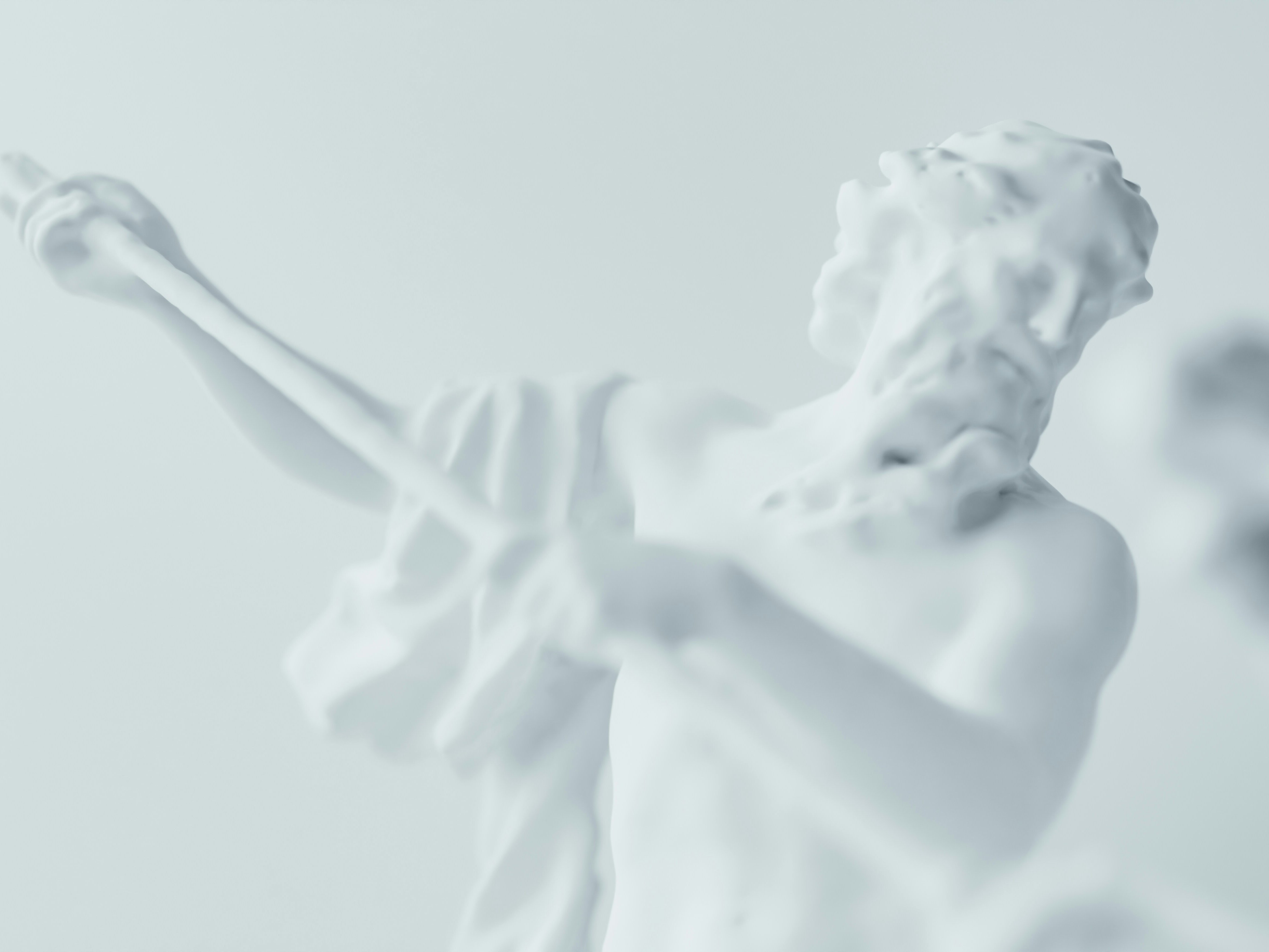 Eine Nahaufnahme einer Statue aus weißem Marmor, die einen bärtigen Mann darstellt, der einen Stab oder Speer hält, mit einer weiteren verschwommenen Gestalt im Vordergrund, alles vor einem hellen Hintergrund.