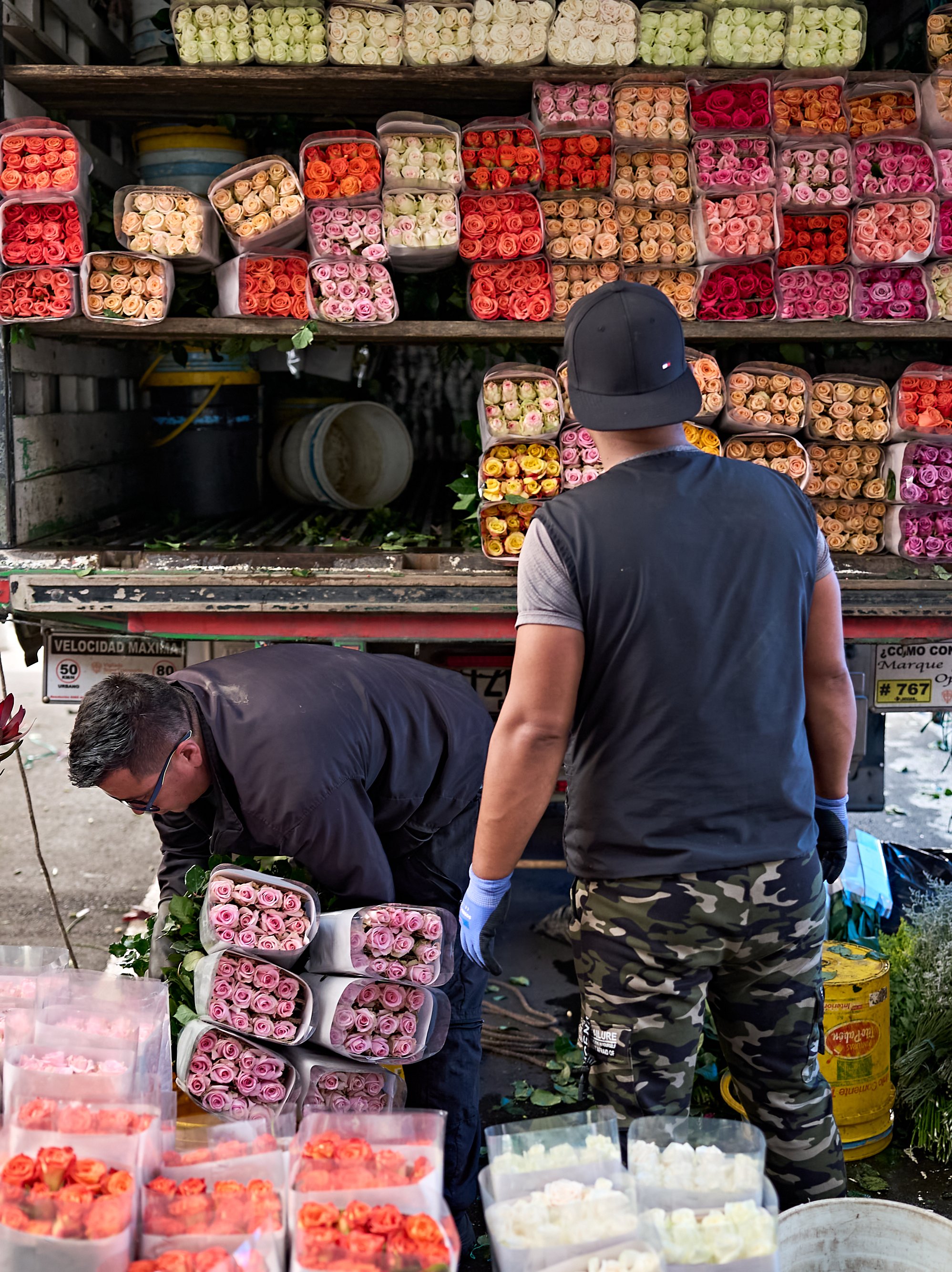 Zwei Arbeiter laden Bündel bunter Rosen vom Heck eines Lieferwagens ab.