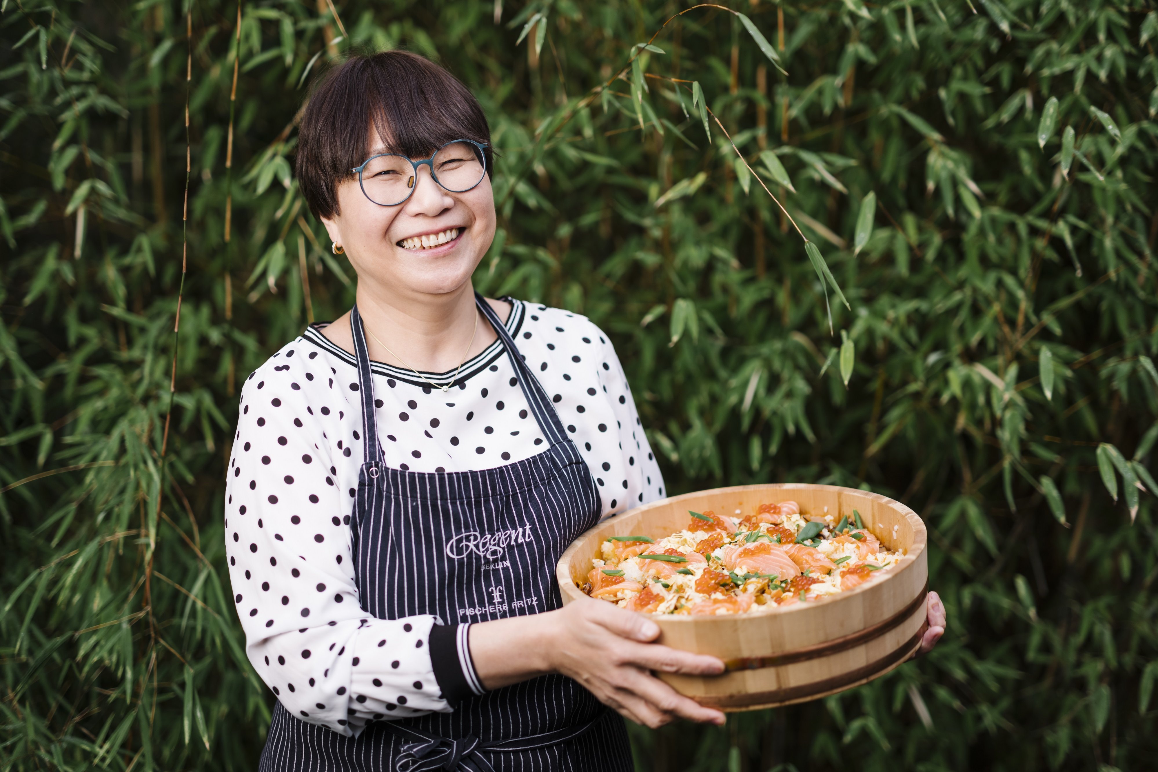 Kotowa Machida holds a large wooden bowl with rice and fish.