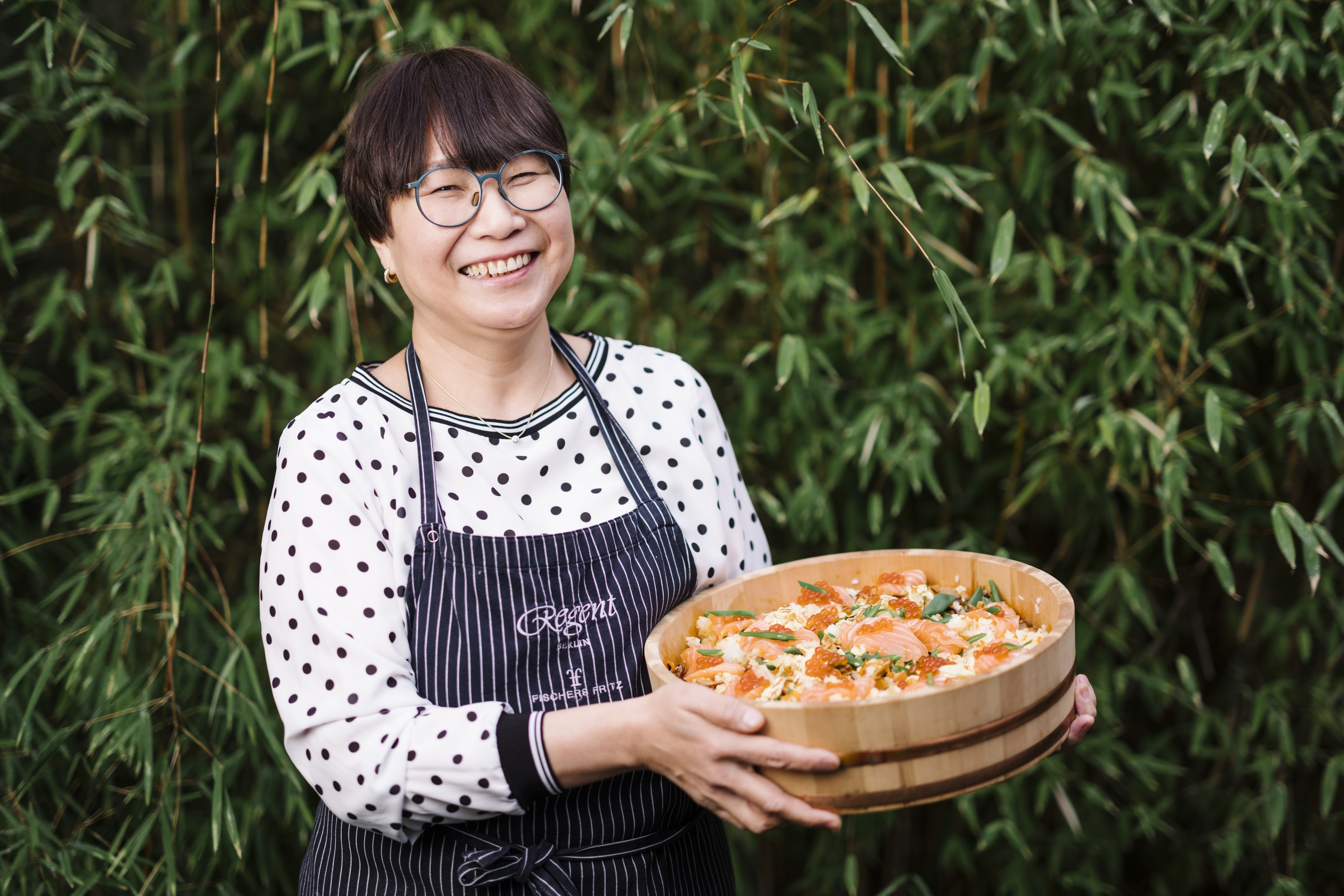 Kotowa Machida hält eine große Holzschüssel mit Reis und Fisch.