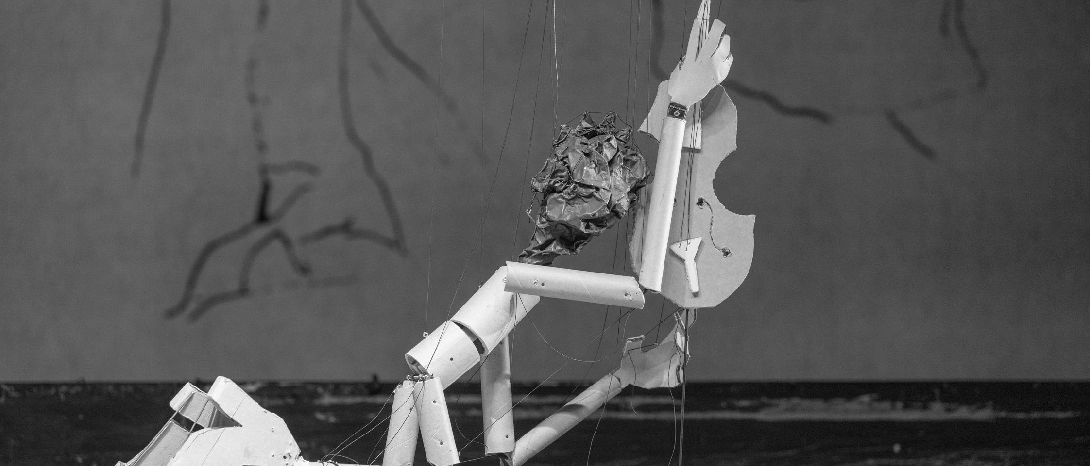 Eine Marionette hält, auf den Knien abgestützt, ein Streichinstrument in die Höhe.