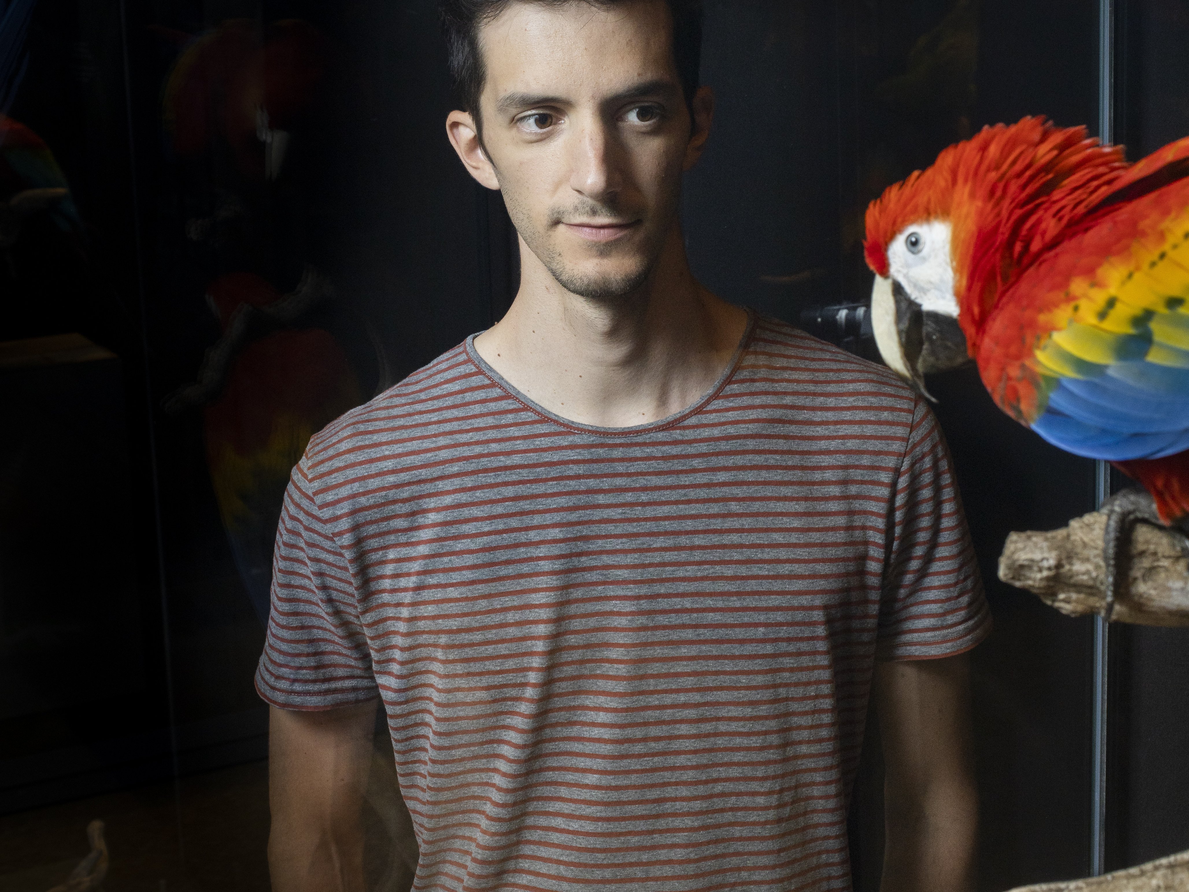 Bruno Delepelaire next to a red parrot.
