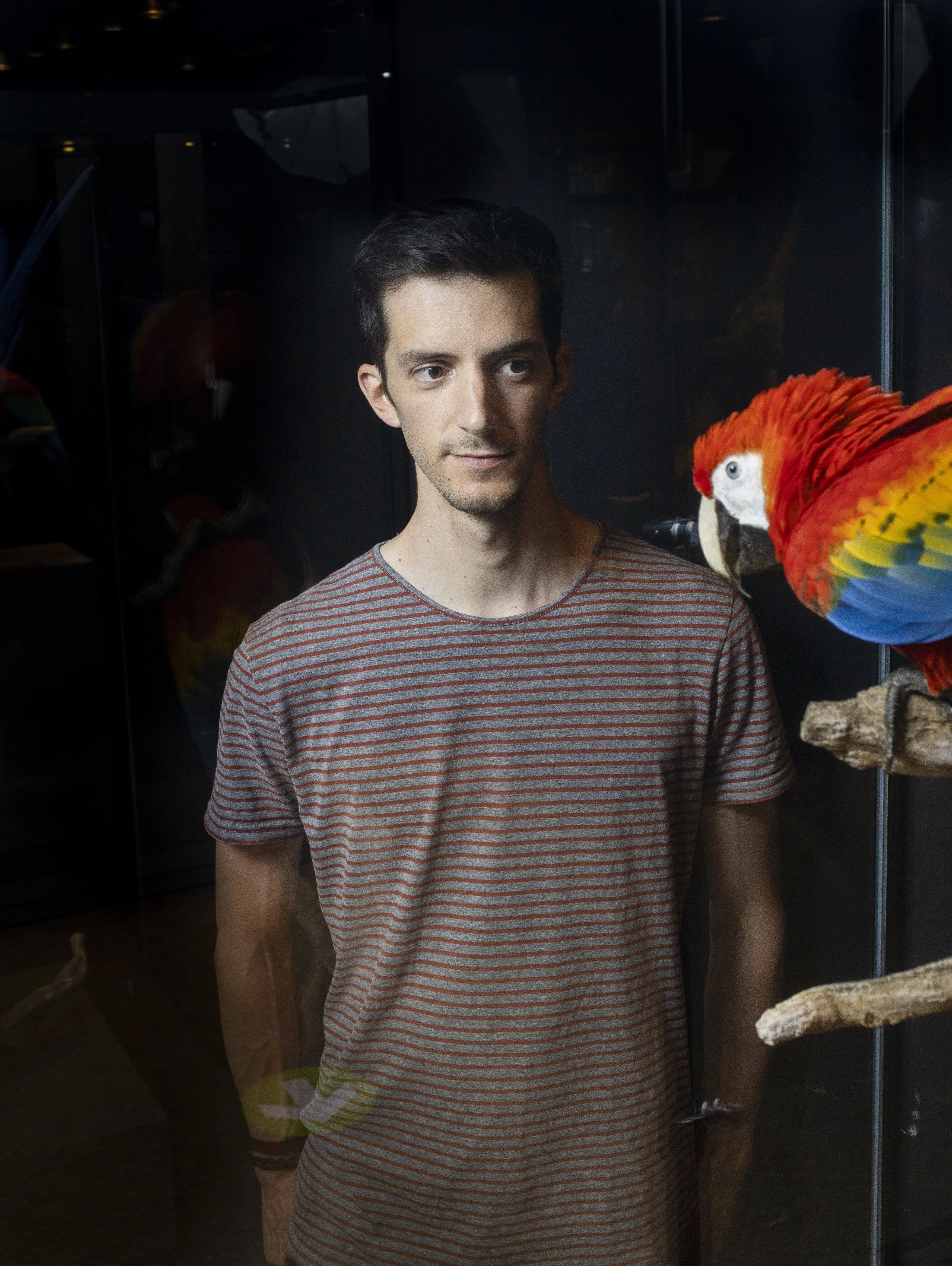 Bruno Delepelaire next to a red parrot.