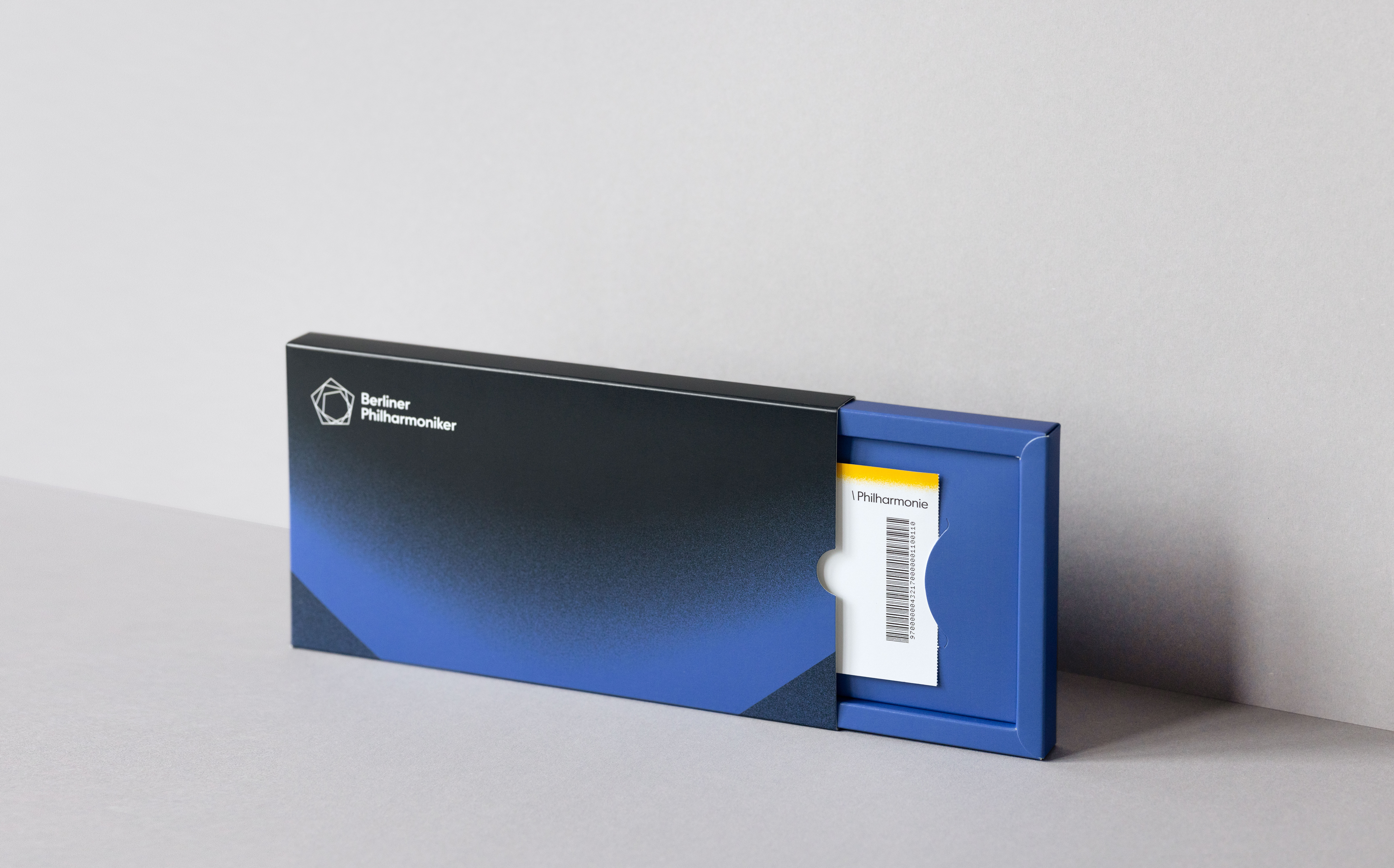 Eine schlichte, schwarz-blaue, rechteckige Schachtel mit der Aufschrift Berliner Philharmoniker ist teilweise geöffnet und gibt den Blick auf eine weiße Karte mit einem Strichcode.
