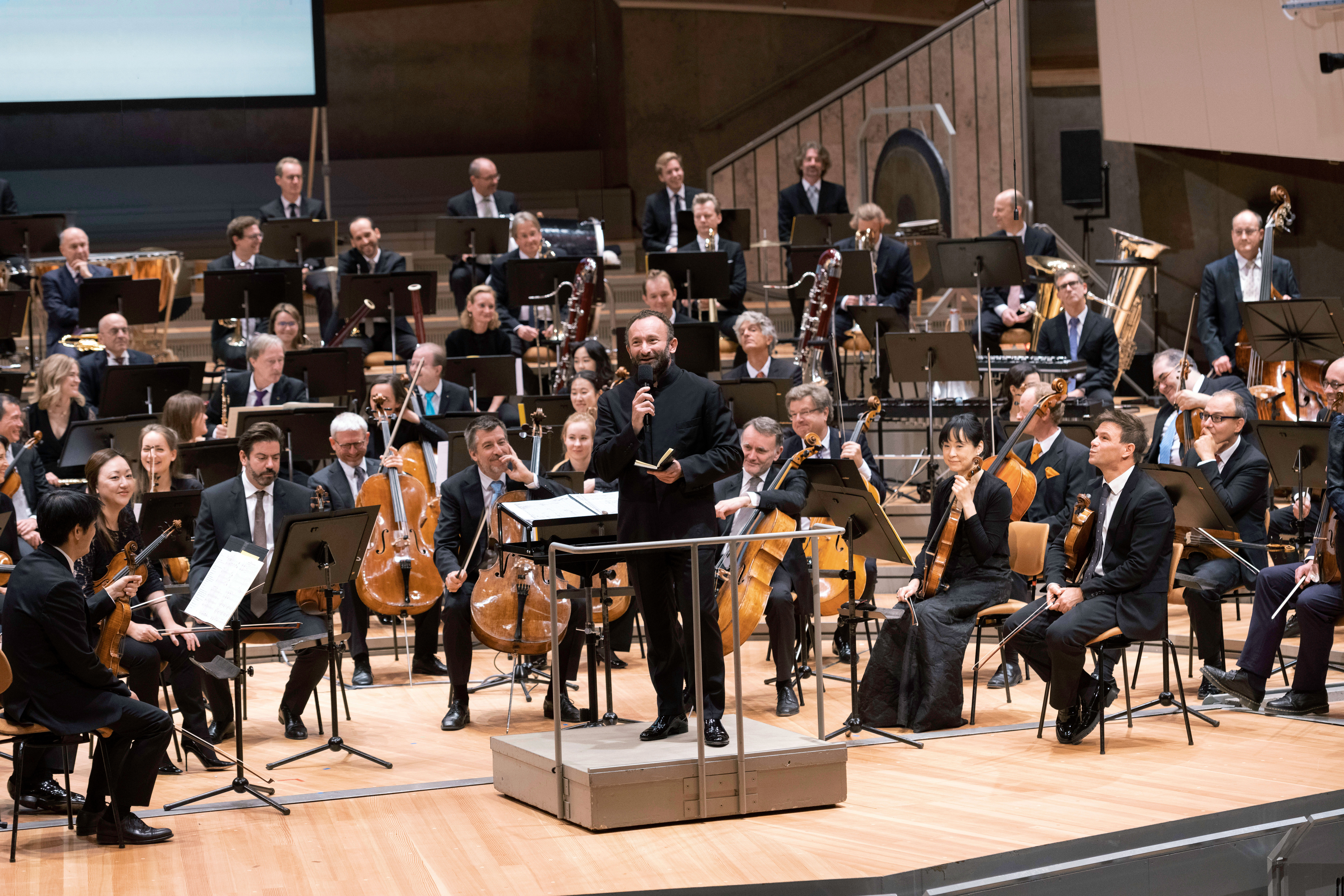 Kirill Petrenko mit Mikrophon vor dem Orchester