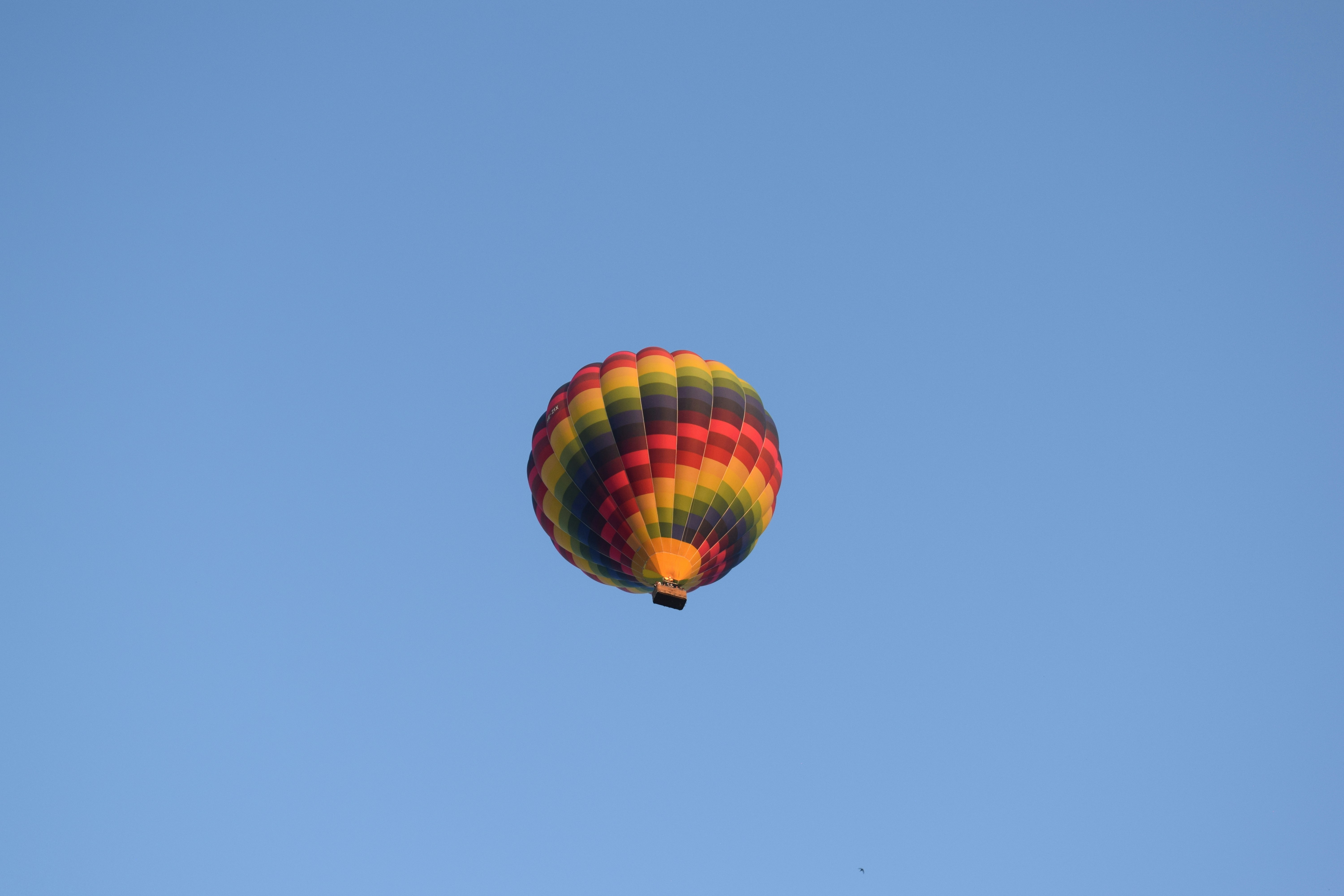 Ein bunter Heißluftballon mit roten, gelben und schwarzen Streifen schwebt am strahlend blauen Himmel.