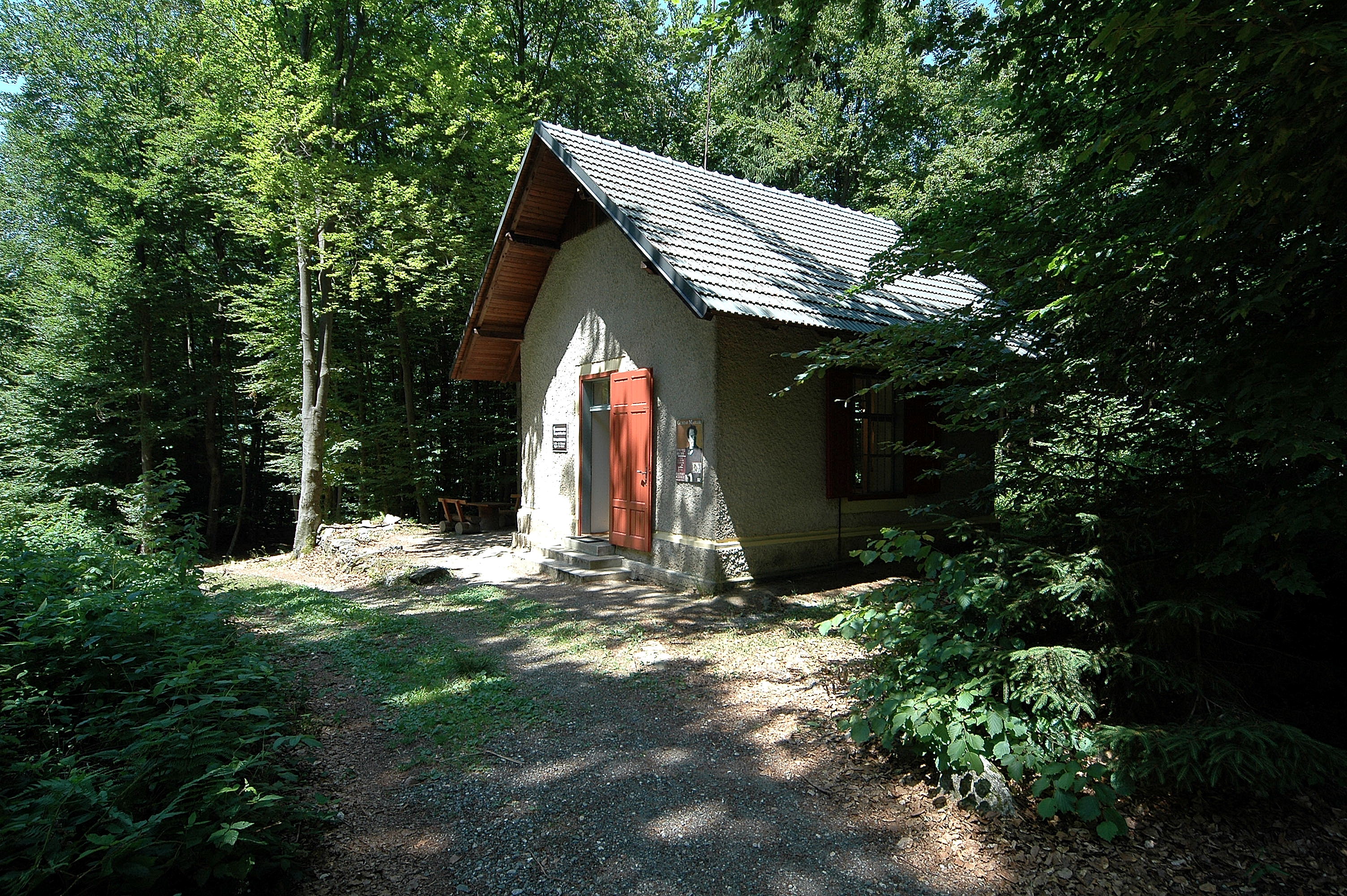 Small, brick-built house with red door surrounded by trees