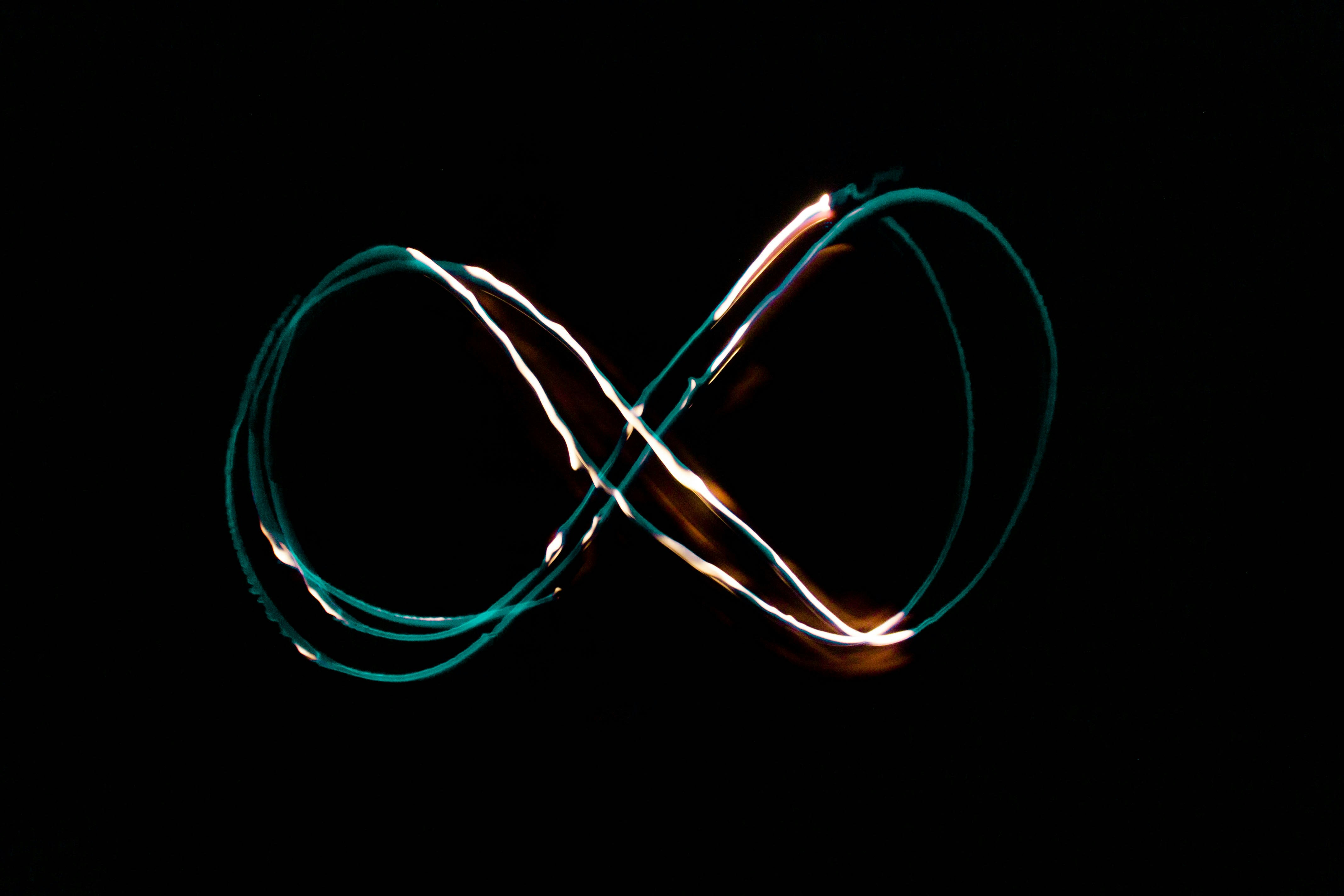 A glowing infinity symbol is drawn with light against a black background, creating bright, colorful trails that loop and intersect in the center.