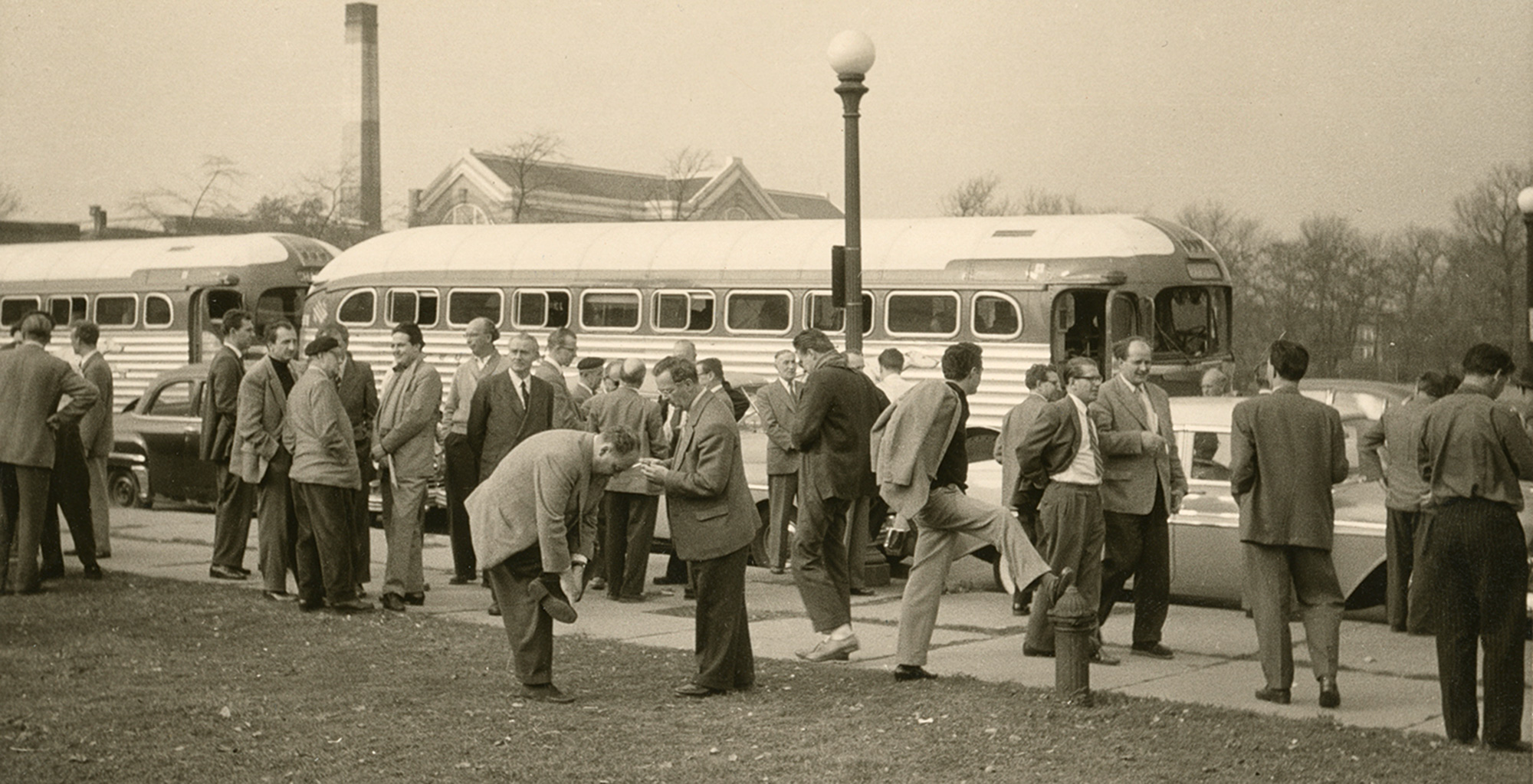 The orchestra members wait next to several buses. Some of them are visibly stretching their legs.