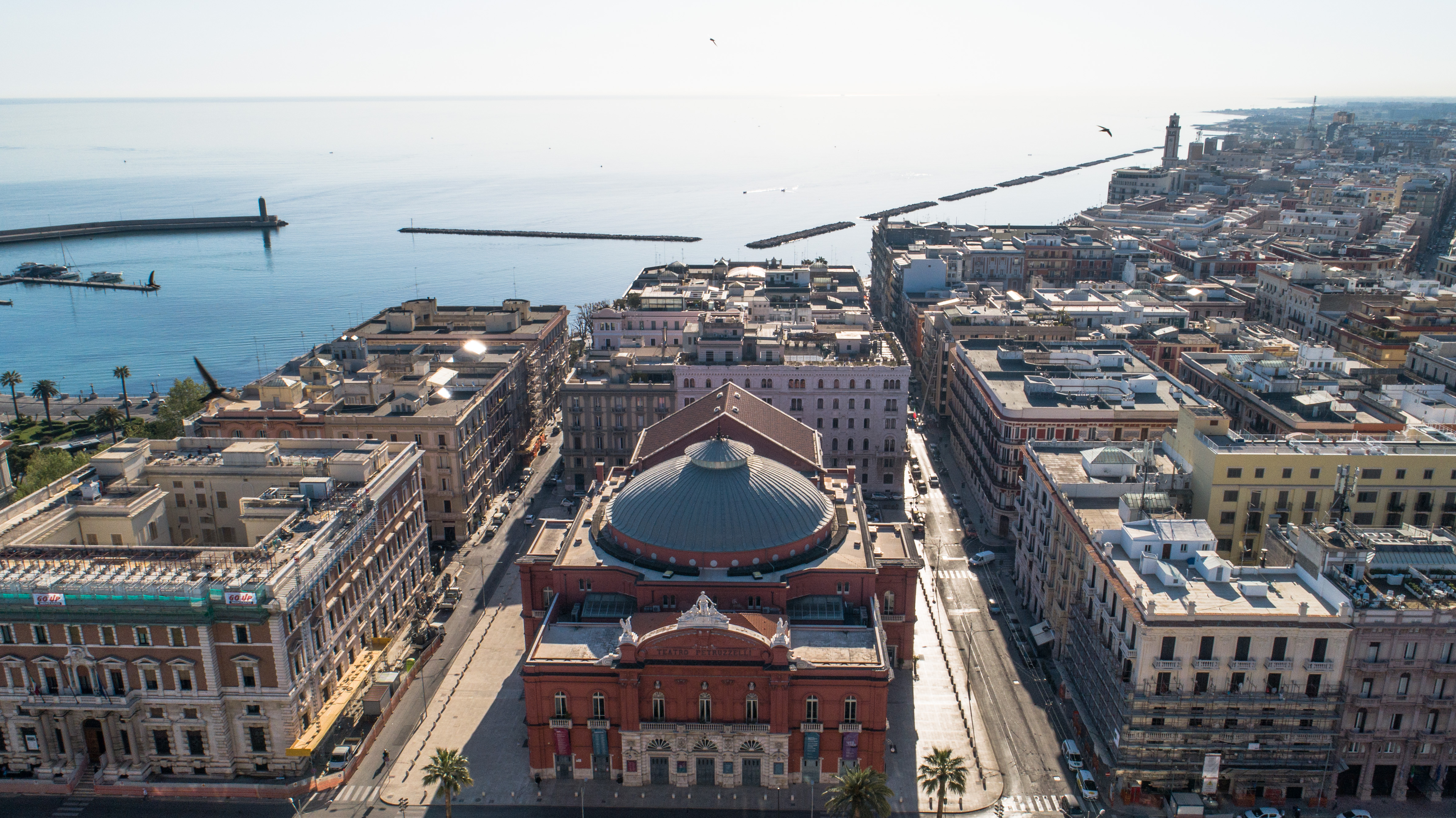 Aerial view of Bari, Italy. The striking red Petruzzelli Theatre can be seen in the centre, surrounded by city buildings, and the Adriatic Sea with breakwaters in the background.