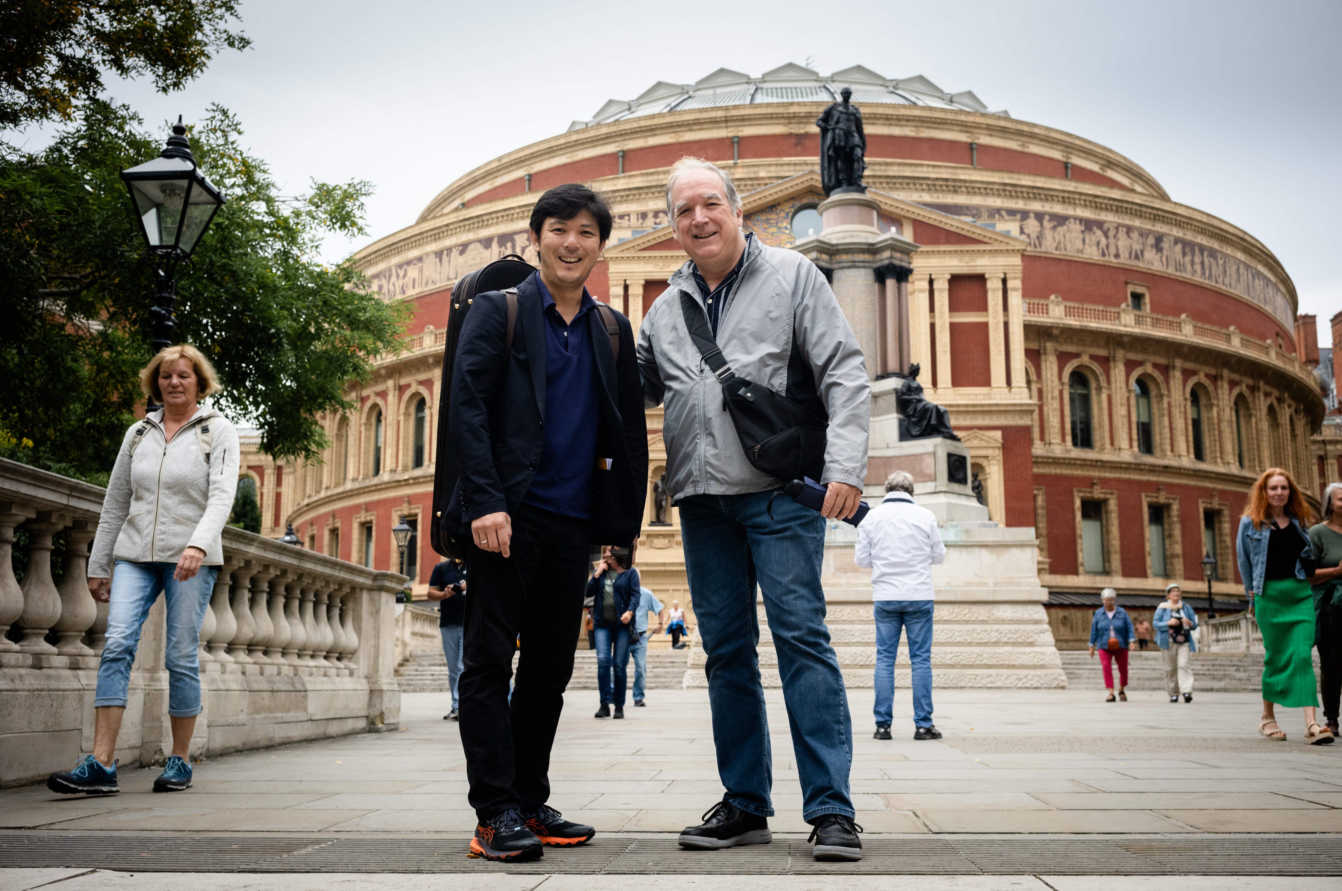 First concertmaster Daishin Kashimoto and violist Matthew Hunter stand in front of the Royal Albert Hall in London and smile for the camera.
