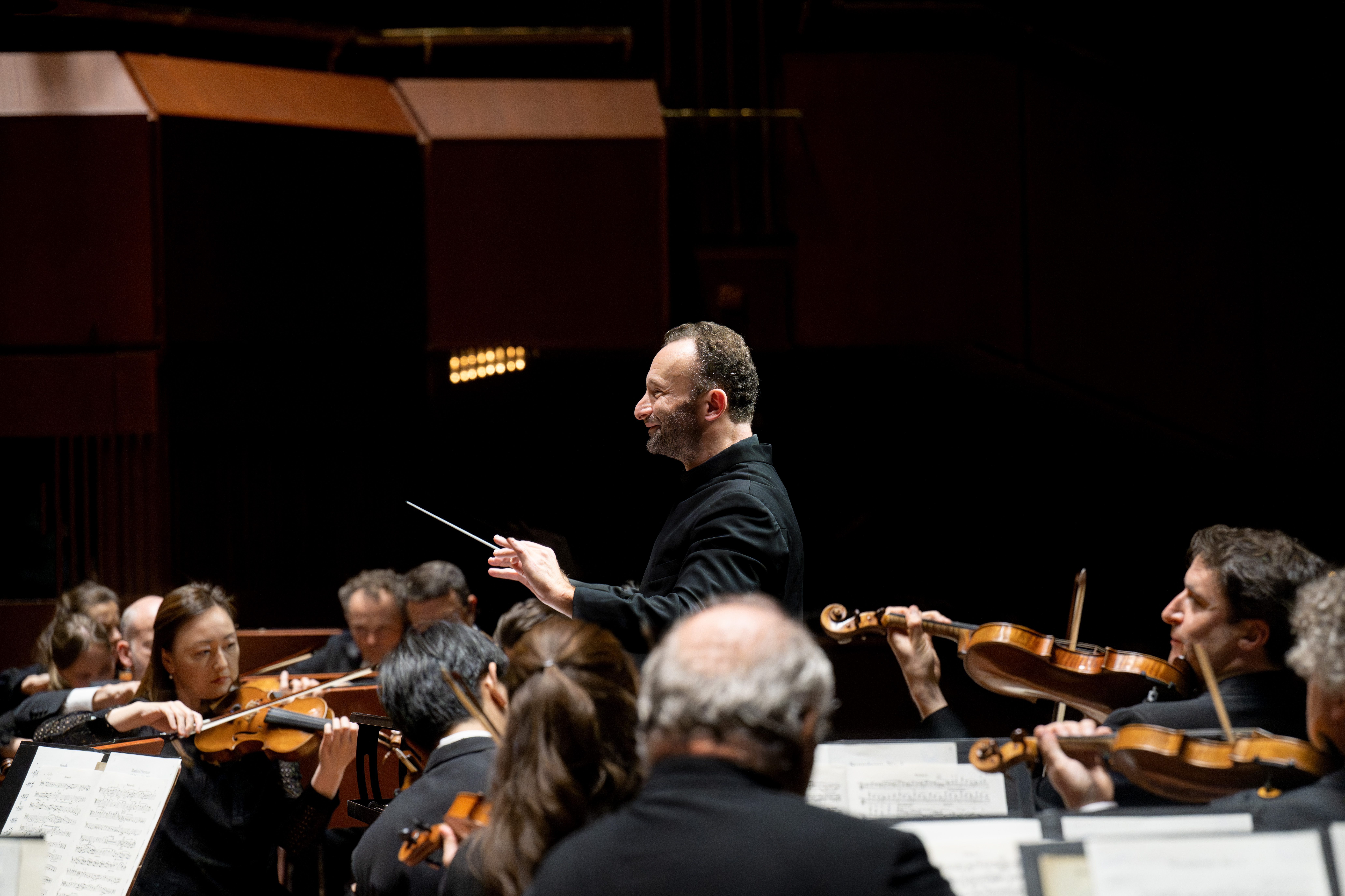 Dirigent Kirill Petrenko leitet das Orchester, während die Musiker konzentriert ihre Streichinstrumente spielen.