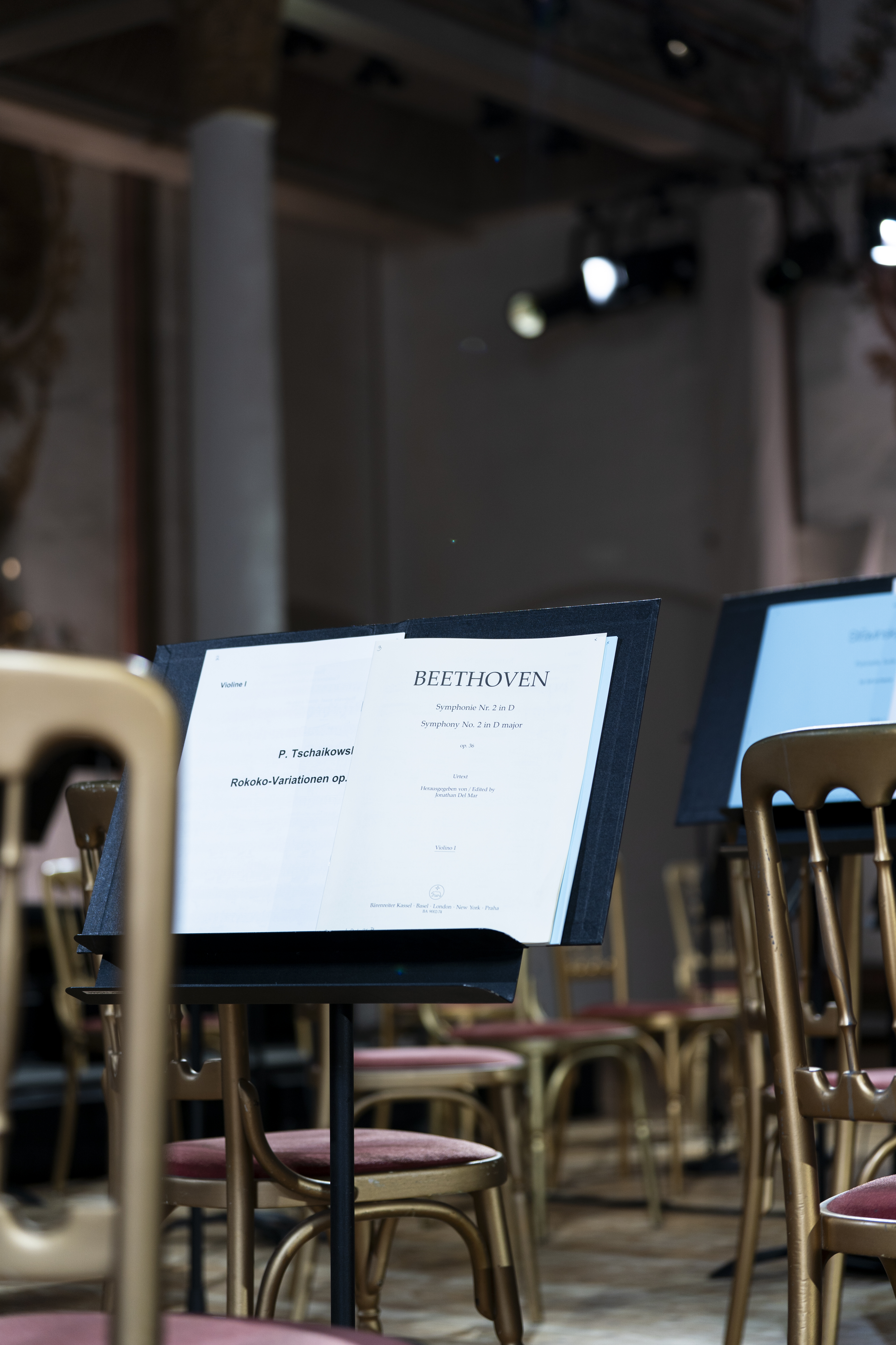 Nahaufnahme eines Notenständers mit Beethoven-Noten in einem leeren Konzertsaal, umgeben von goldenen und roten Stuhlreihen bei gedämpftem Licht.