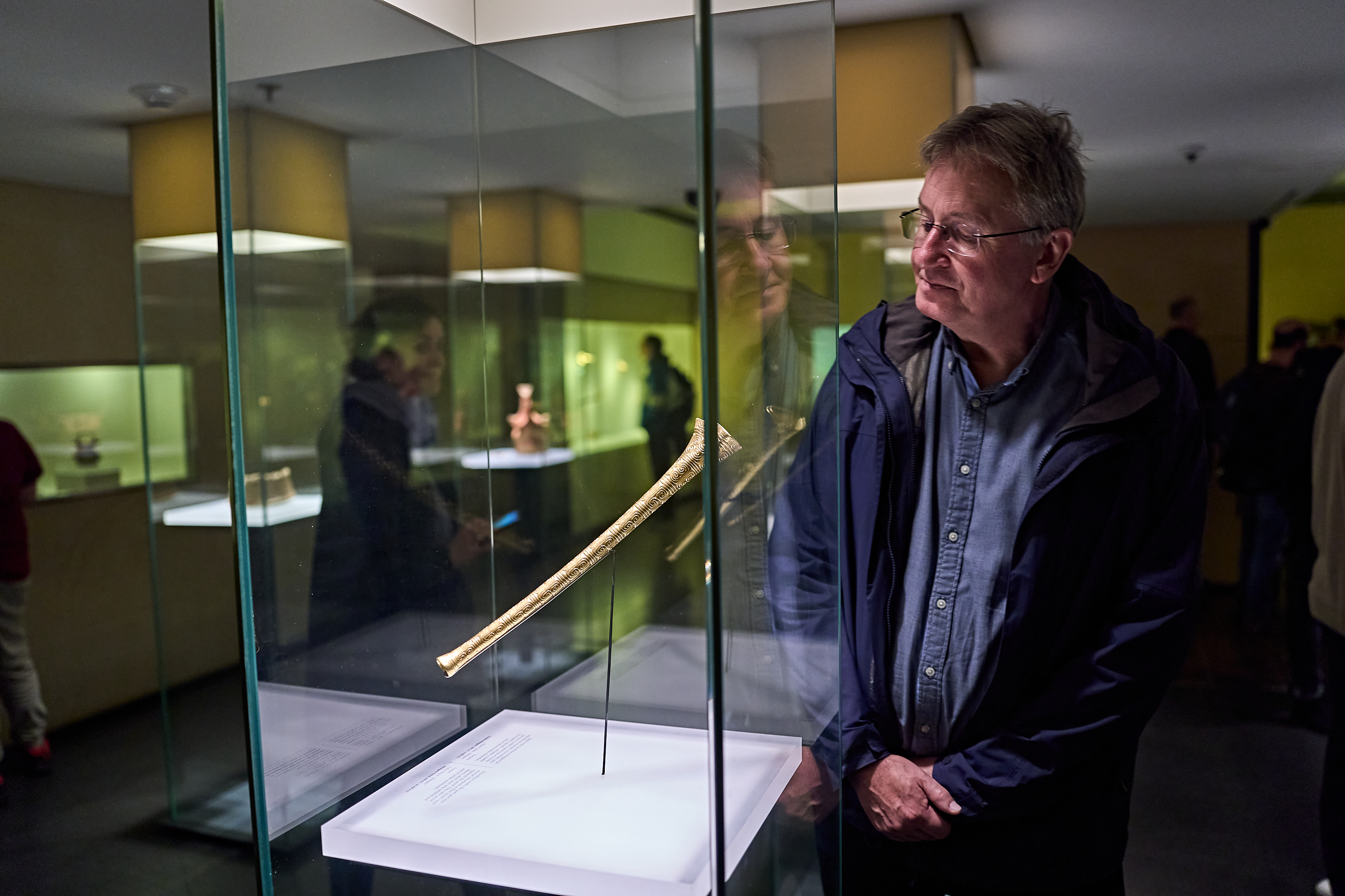 Ein Mann mit Brille betrachtet ein langes, schmales, goldenes Exponat, das in einer Glasvitrine ausgestellt ist.