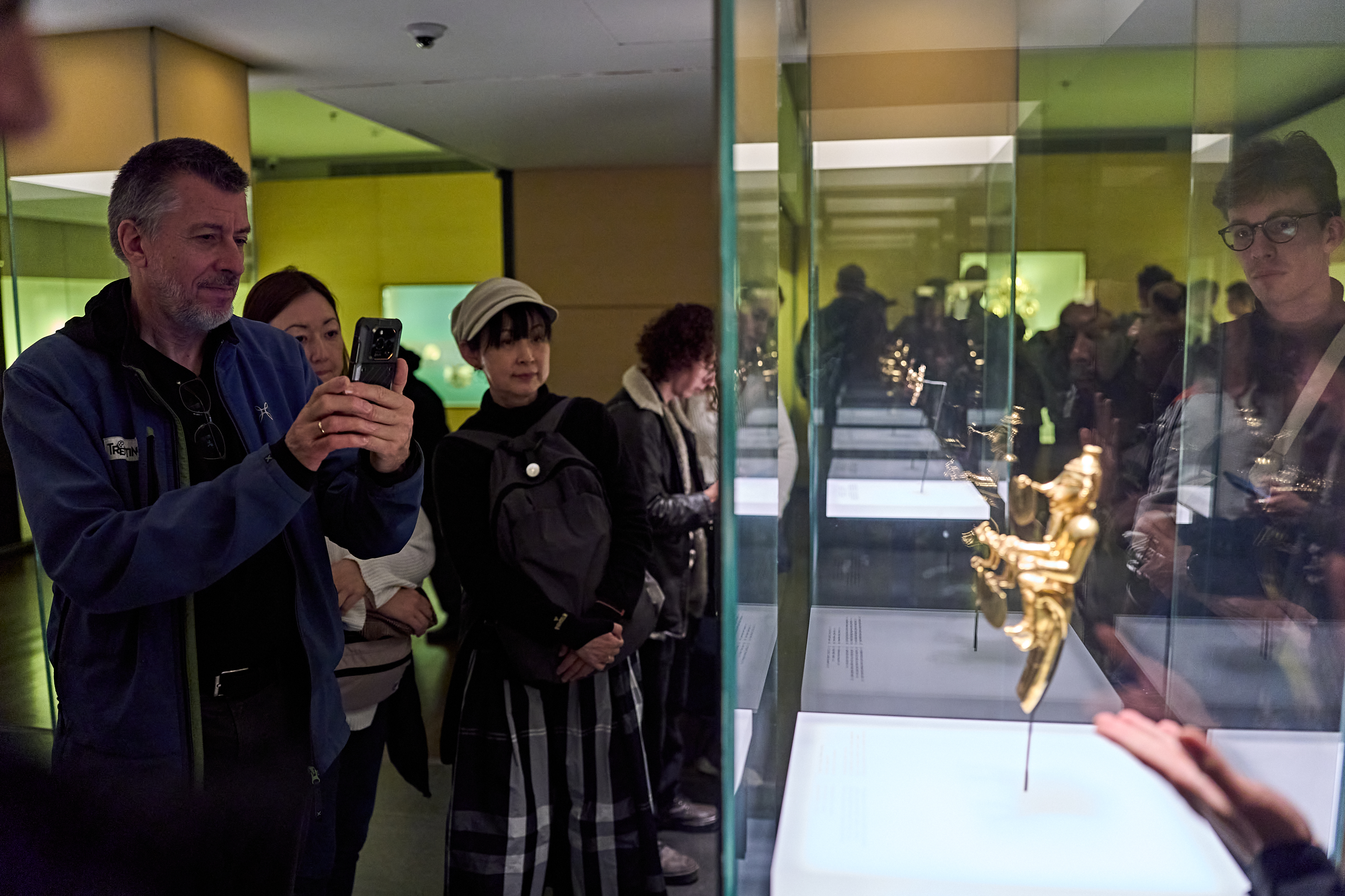 Besucher eines Museums betrachten ein kleines goldenes Exponat, das in einer Glasvitrine ausgestellt ist.
