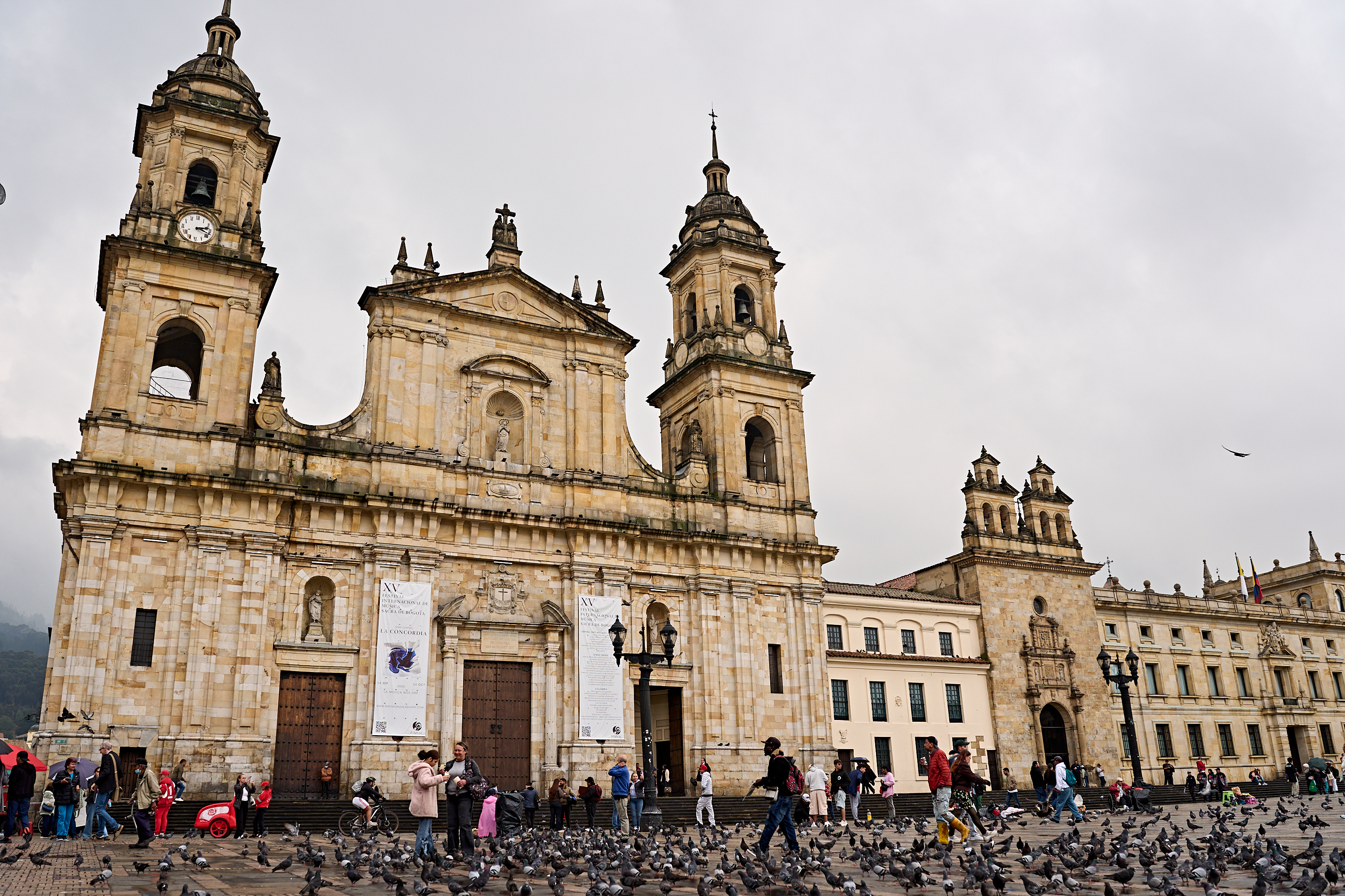Die Primatialkathedrale von Bogotá auf der Plaza de Bolívar mit Passanten und einem großen Schwarm Tauben im Vordergrund.