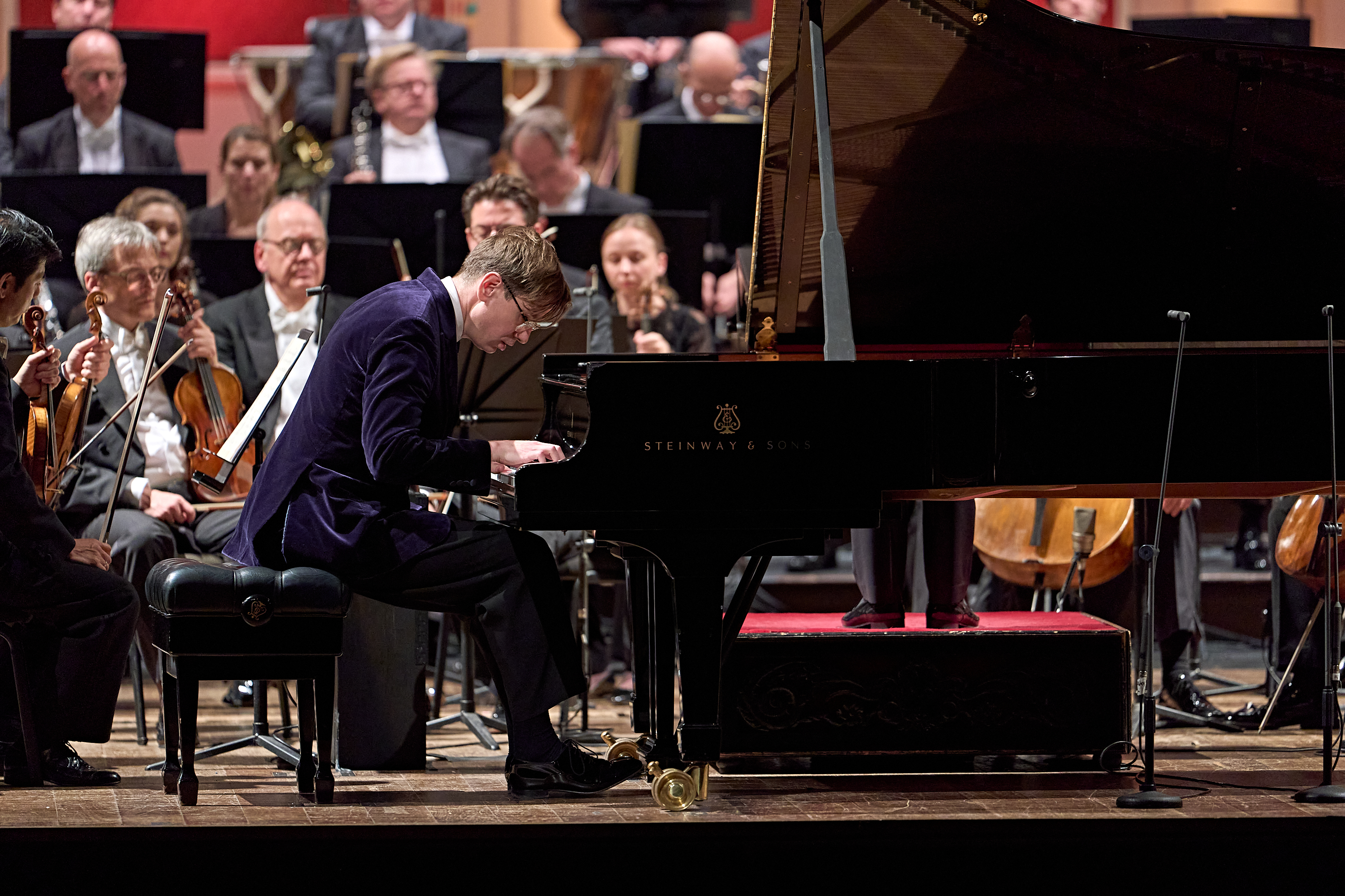 Ein Pianist in einer dunkelblauen Samtjacke spielt während eines Orchesterkonzerts auf einem Steinway-Flügel.